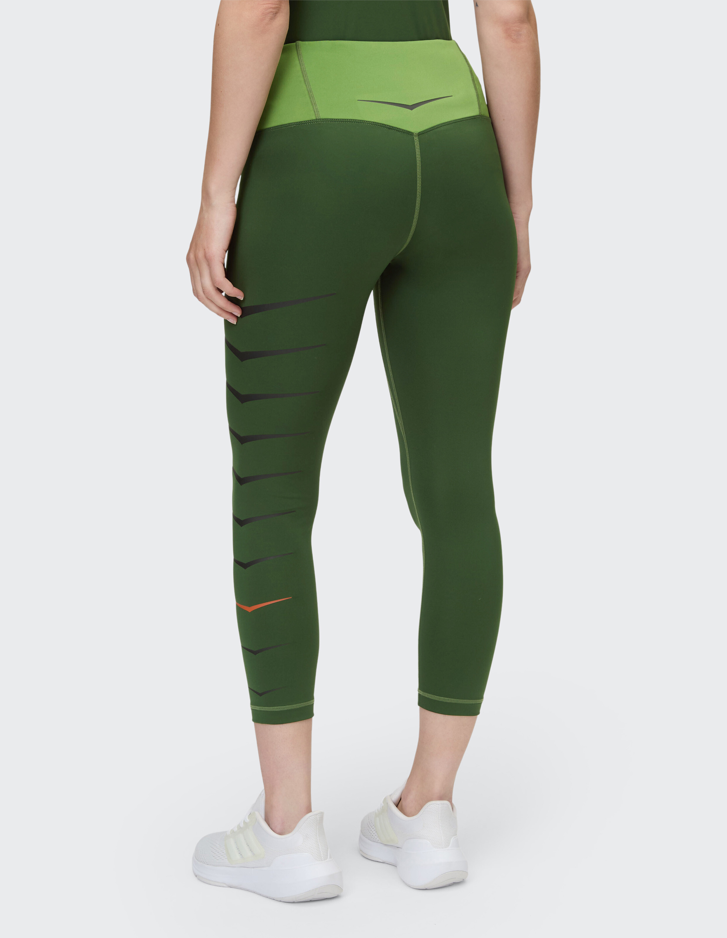 Frau trägt olivgrüne, hoch taillierte, kurze Leggings mit Chevron-Print.
