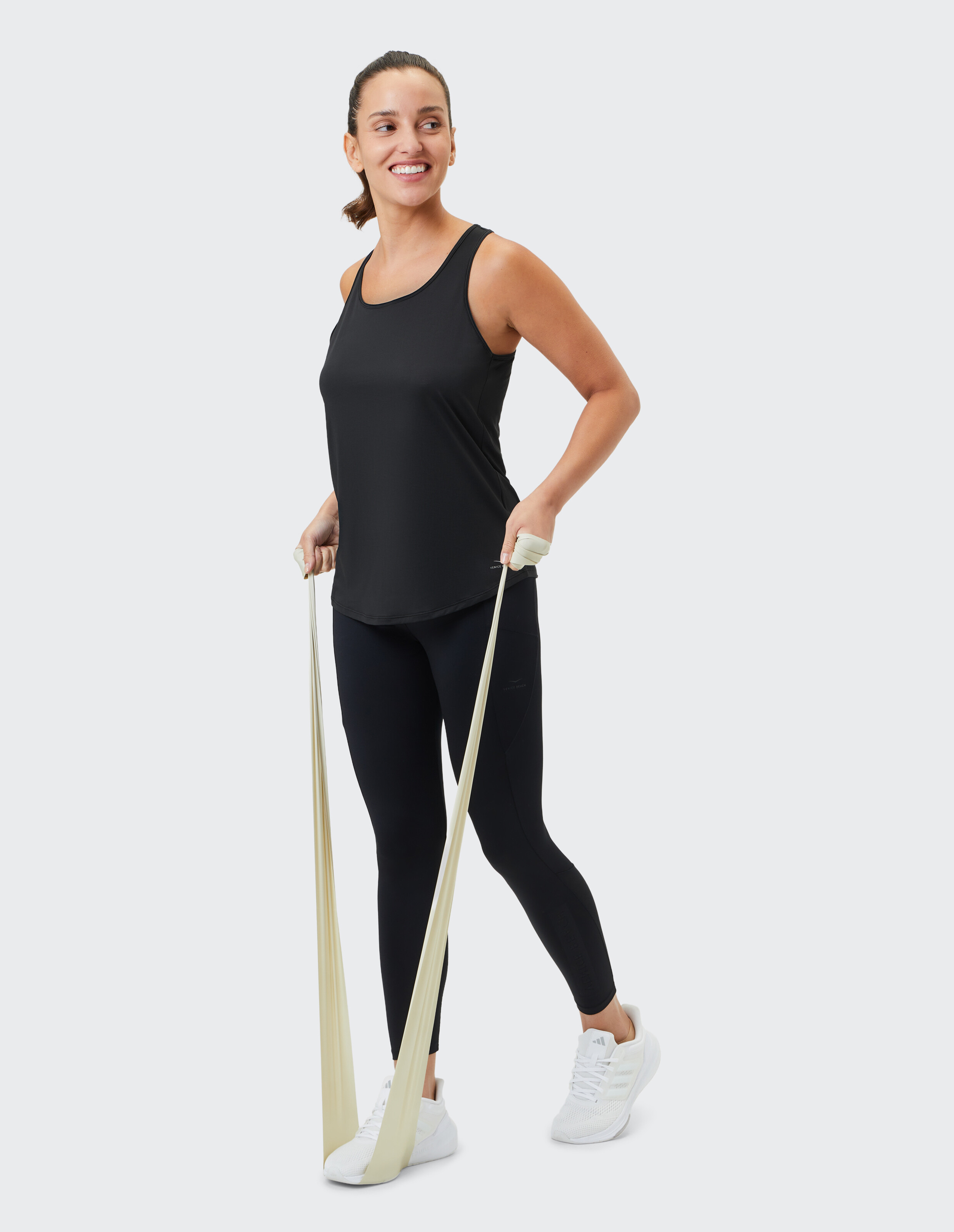 Frau in schwarzem Tanktop und Leggings trainiert mit einem Widerstandsband.