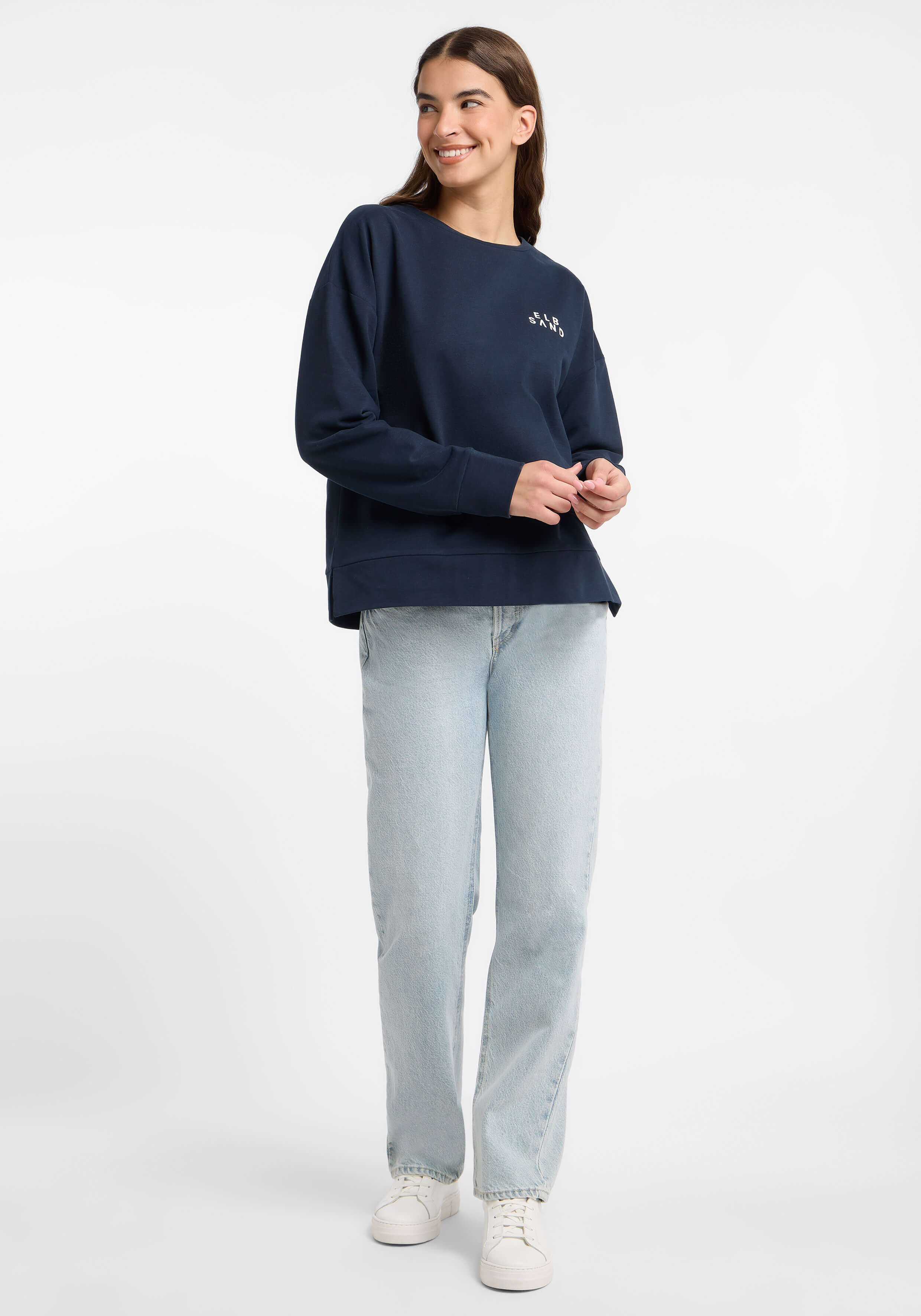 Frau trägt ein dunkelblaues ELBSAND-Sweatshirt und hellblaue Jeans für einen lässigen Look.