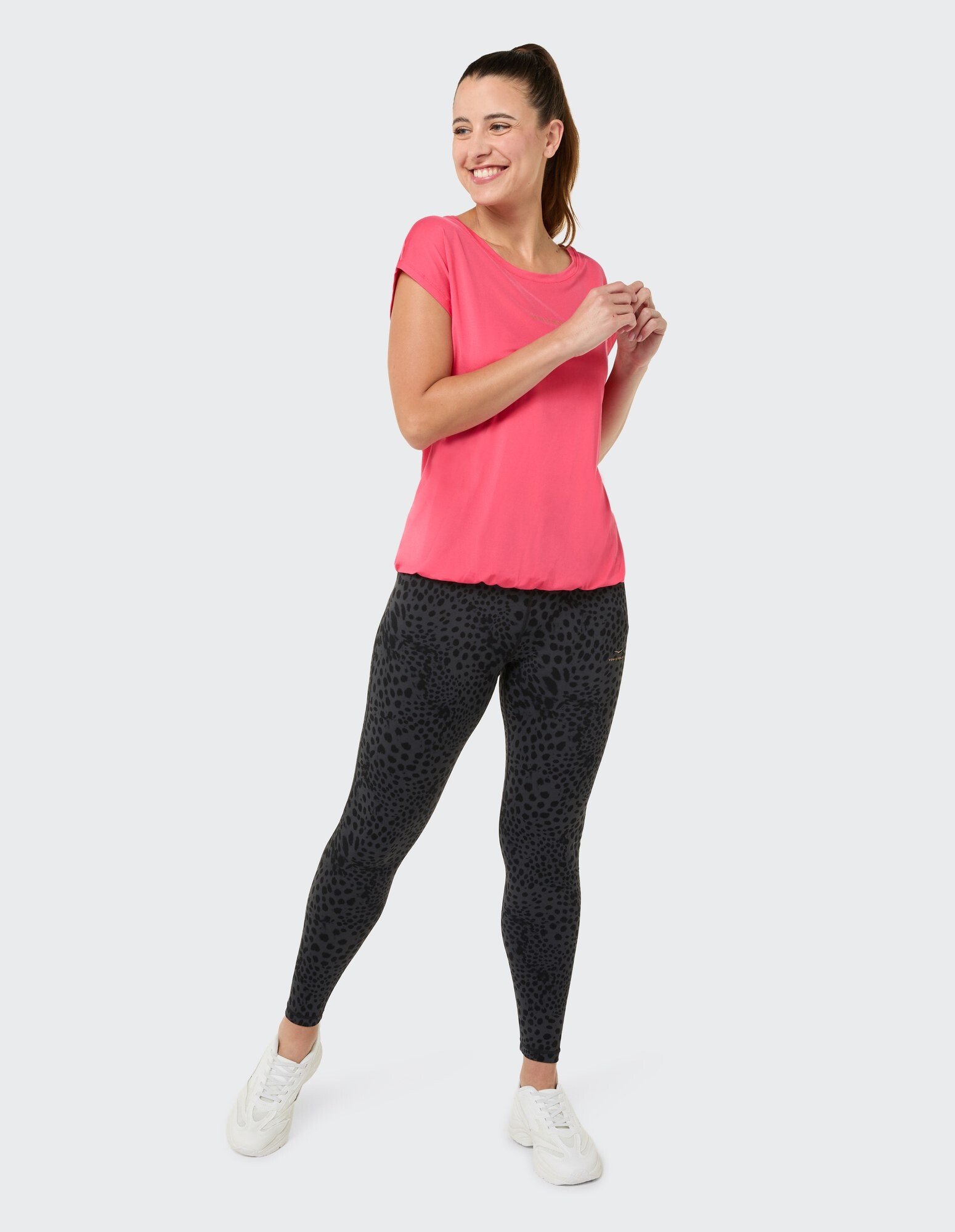 Frau in rosa Top und schwarzen Leggings mit Leopardenmuster, lächelnd.