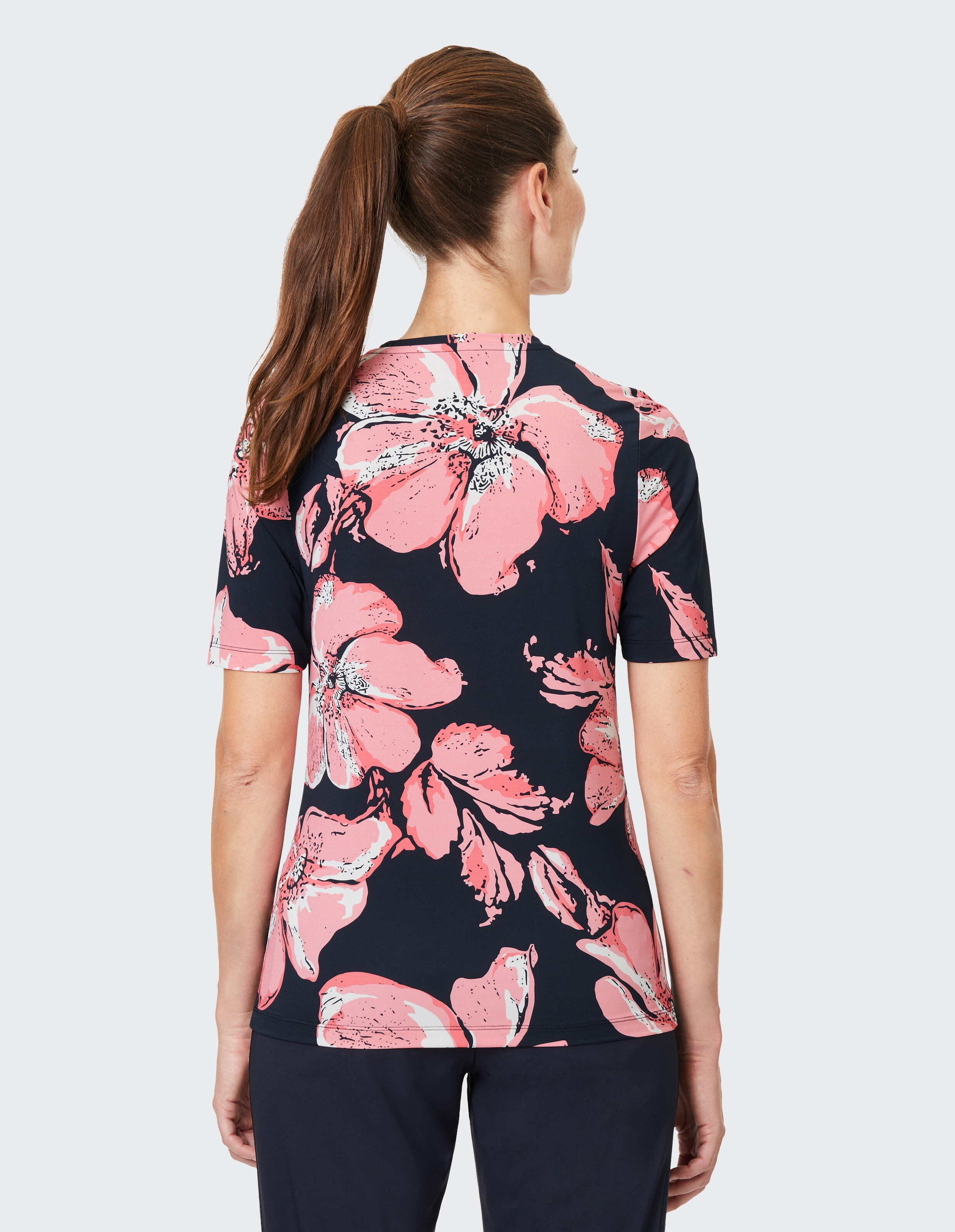 Rückansicht einer Frau in einem kurzärmeligen Oberteil mit Blumendruck und rosa Blumen auf Marineblau.