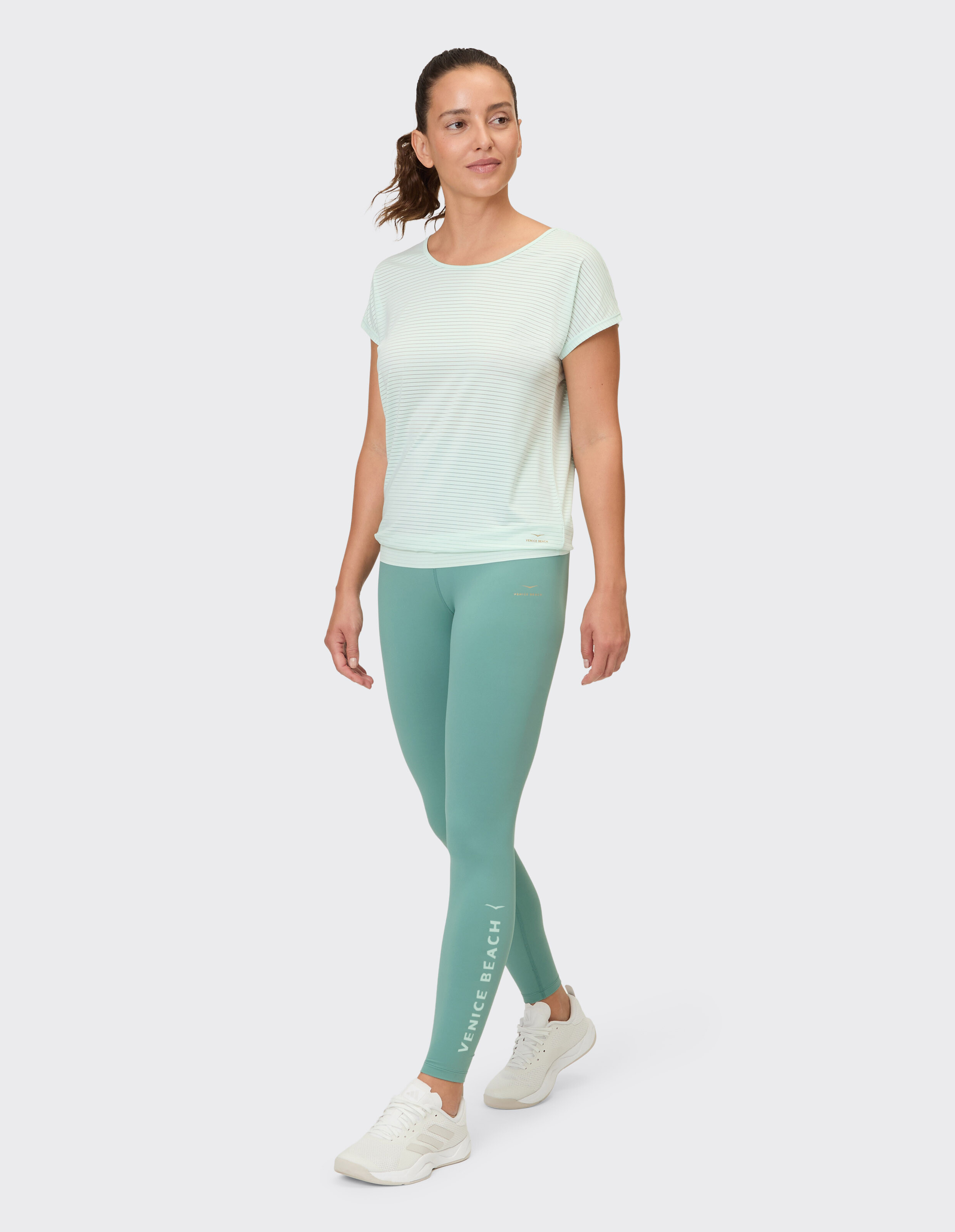 Frau trägt ein hellgrün gestreiftes Oberteil und blaugrüne Leggings für lässige Aktivkleidung.