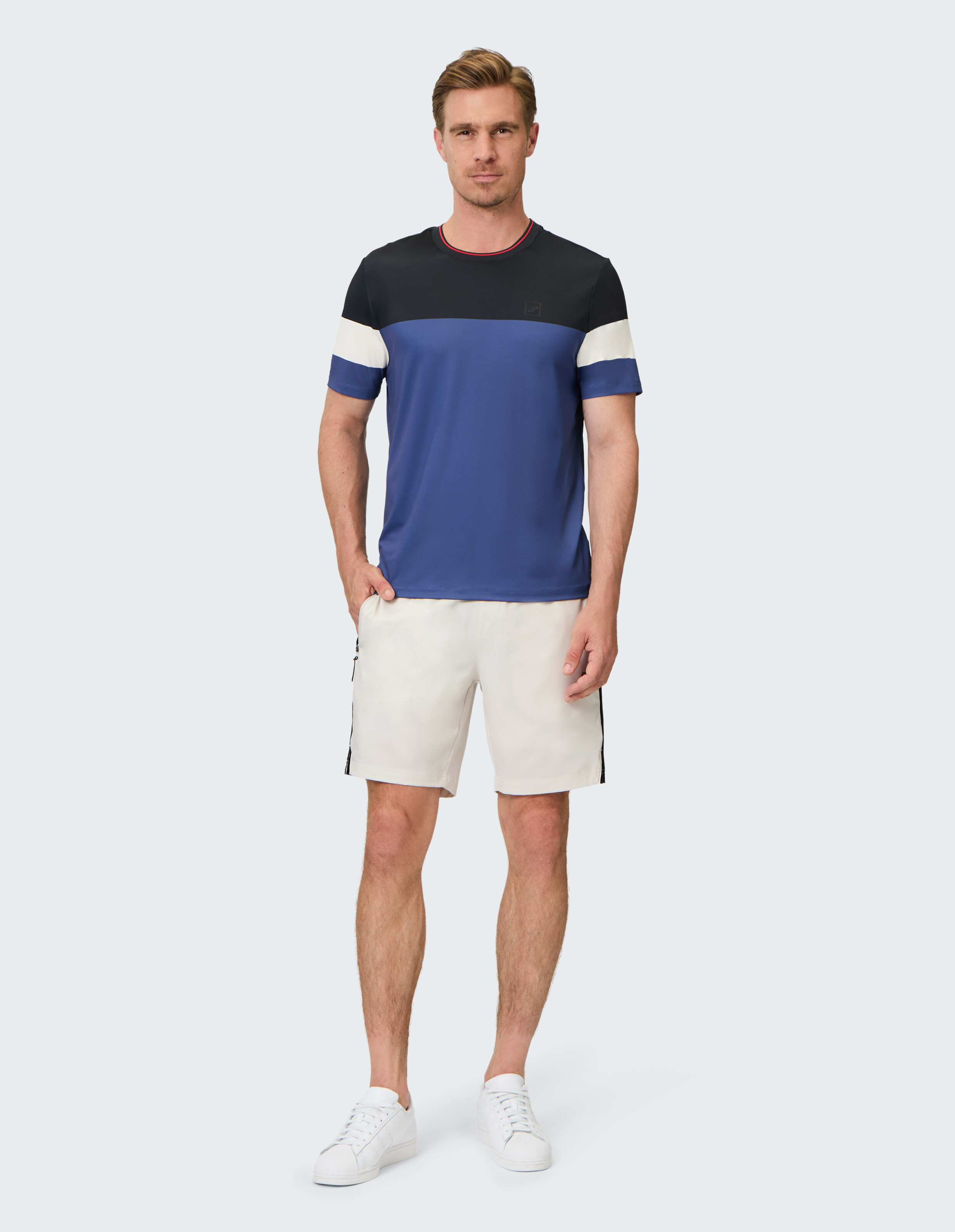 Mann trägt ein blau-schwarzes Farbblock-T-Shirt mit weißen Shorts und Turnschuhen.