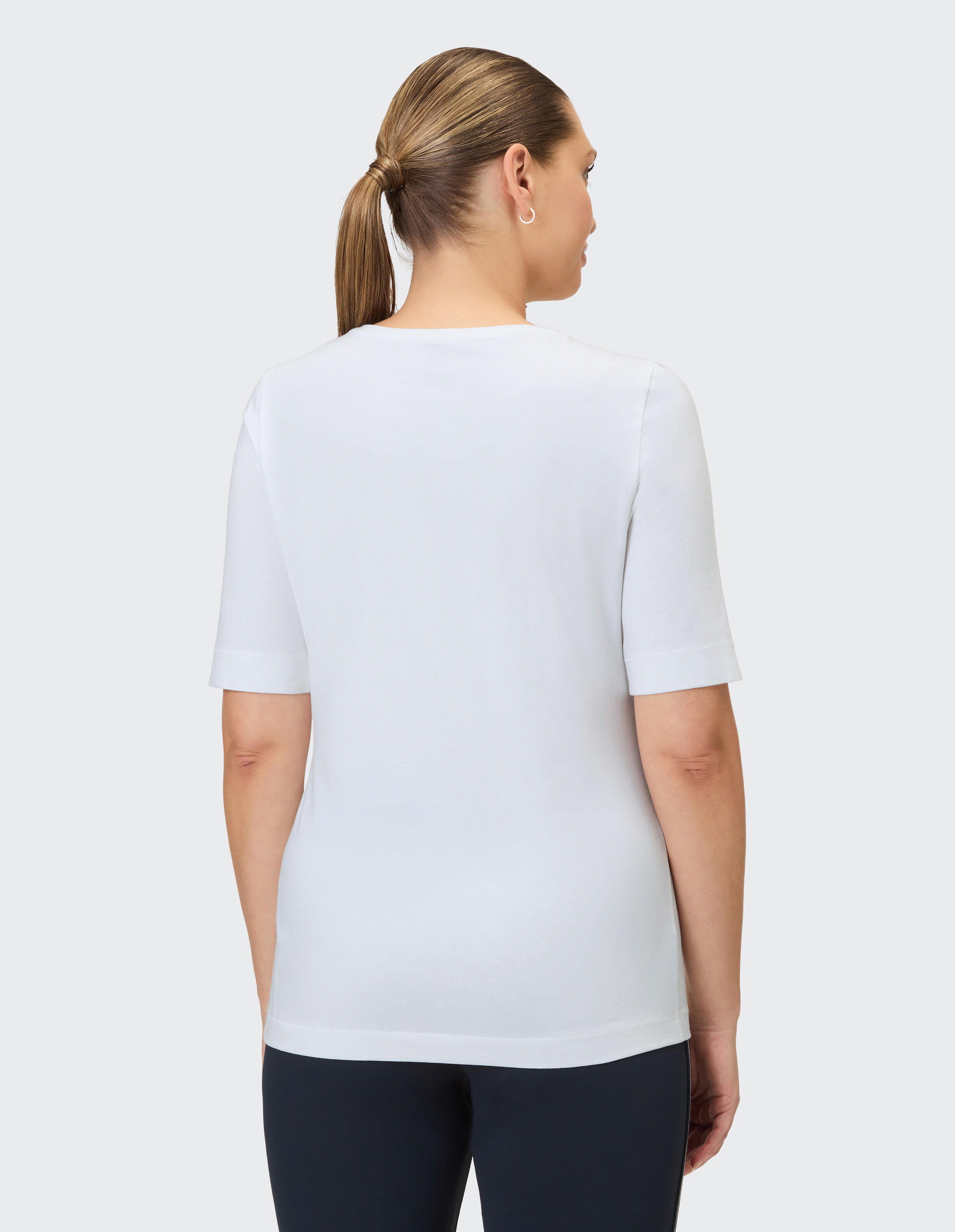Rückenansicht einer Frau in einem kurzärmeligen weißen T-Shirt und einer dunklen Hose.
