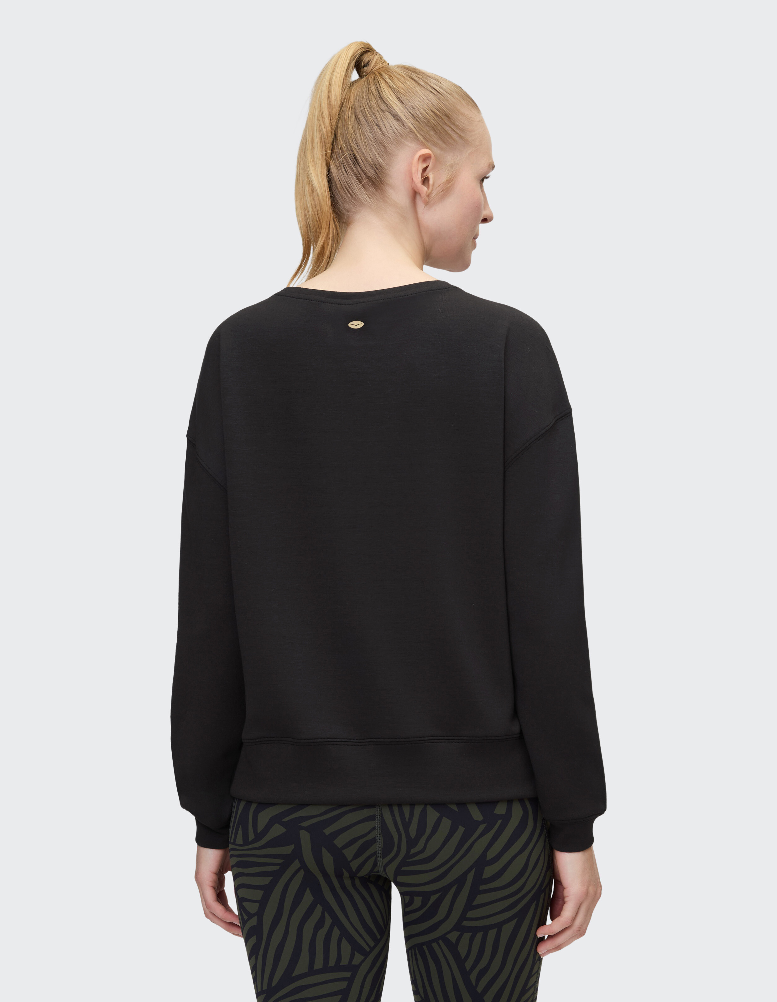 Frau trägt ein gemütliches schwarzes ELBSAND-Sweatshirt mit gemusterten Leggings.