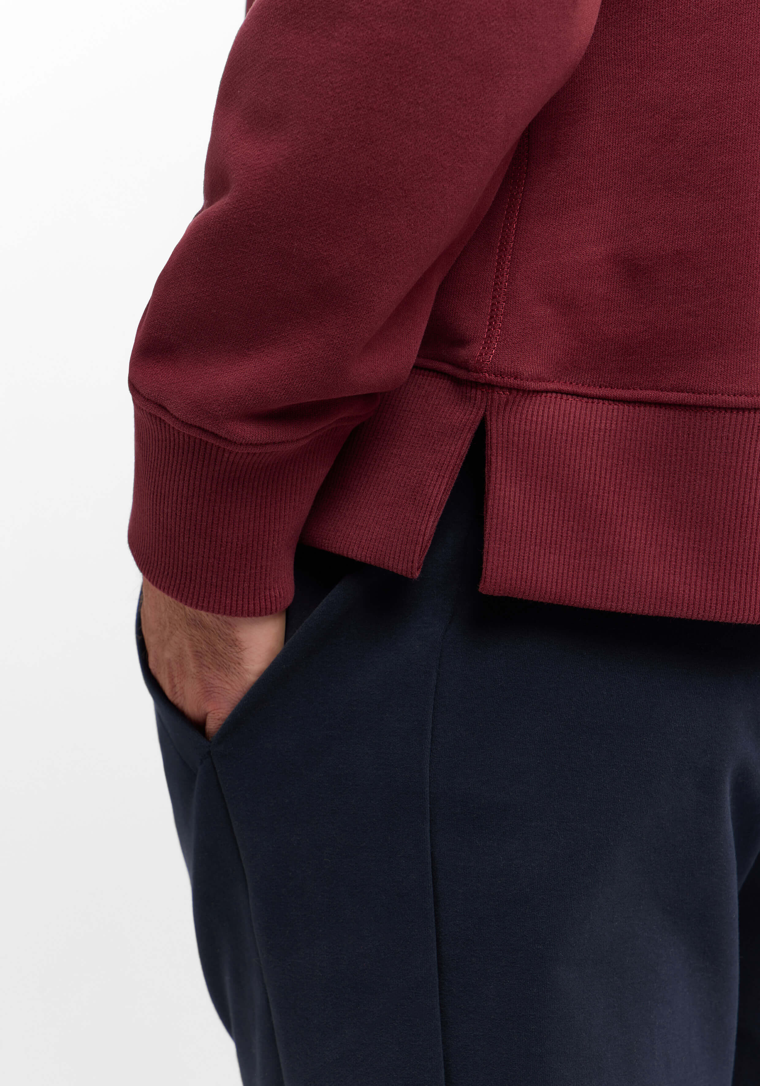 Nahaufnahme eines burgunderfarbenen Sweatshirts mit Seitenschlitzen gepaart mit einer dunkelblauen Freizeithose.