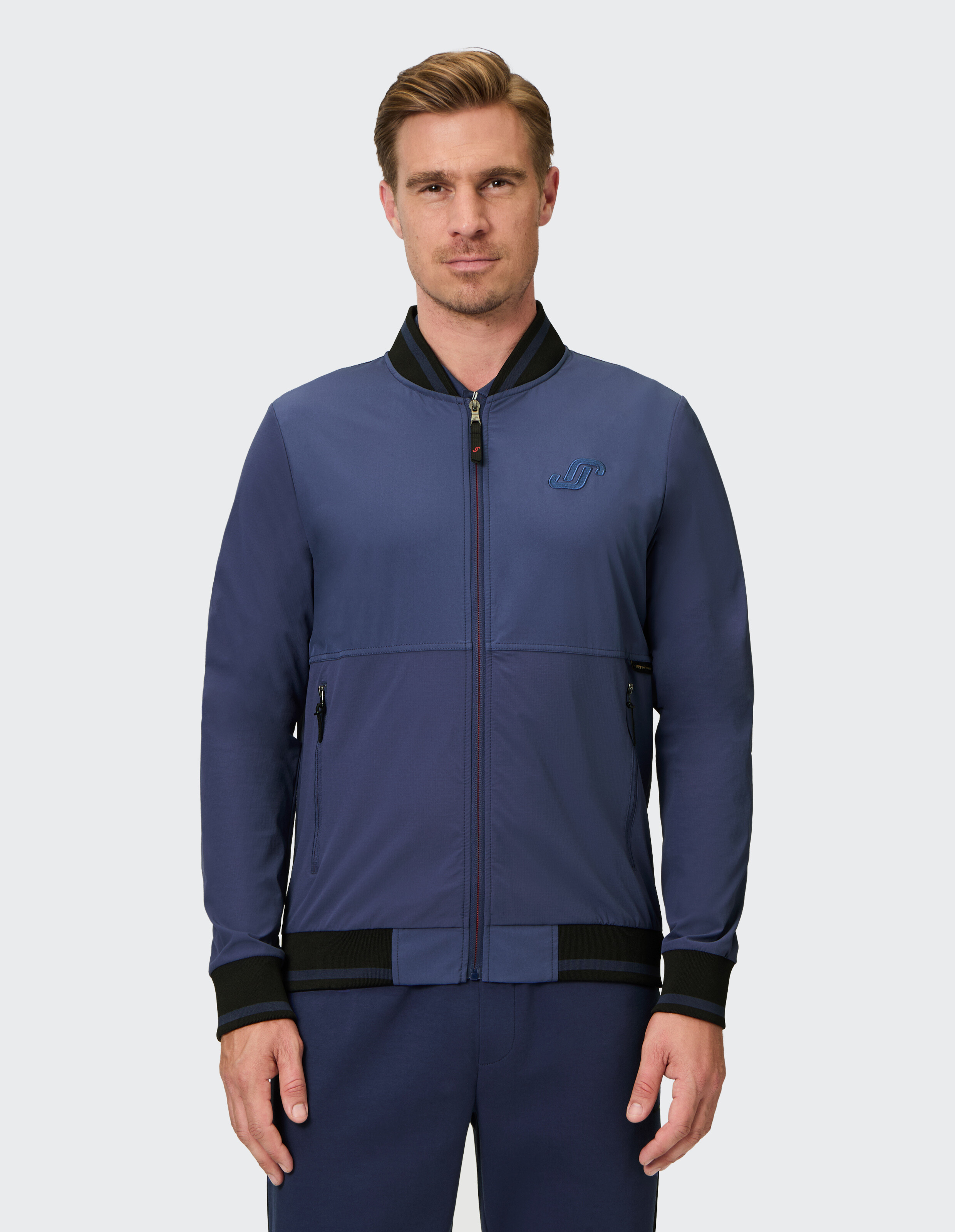 Mann trägt eine blaue, legere Bomberjacke mit schwarzem Rippstrickbesatz und Reißverschluss.