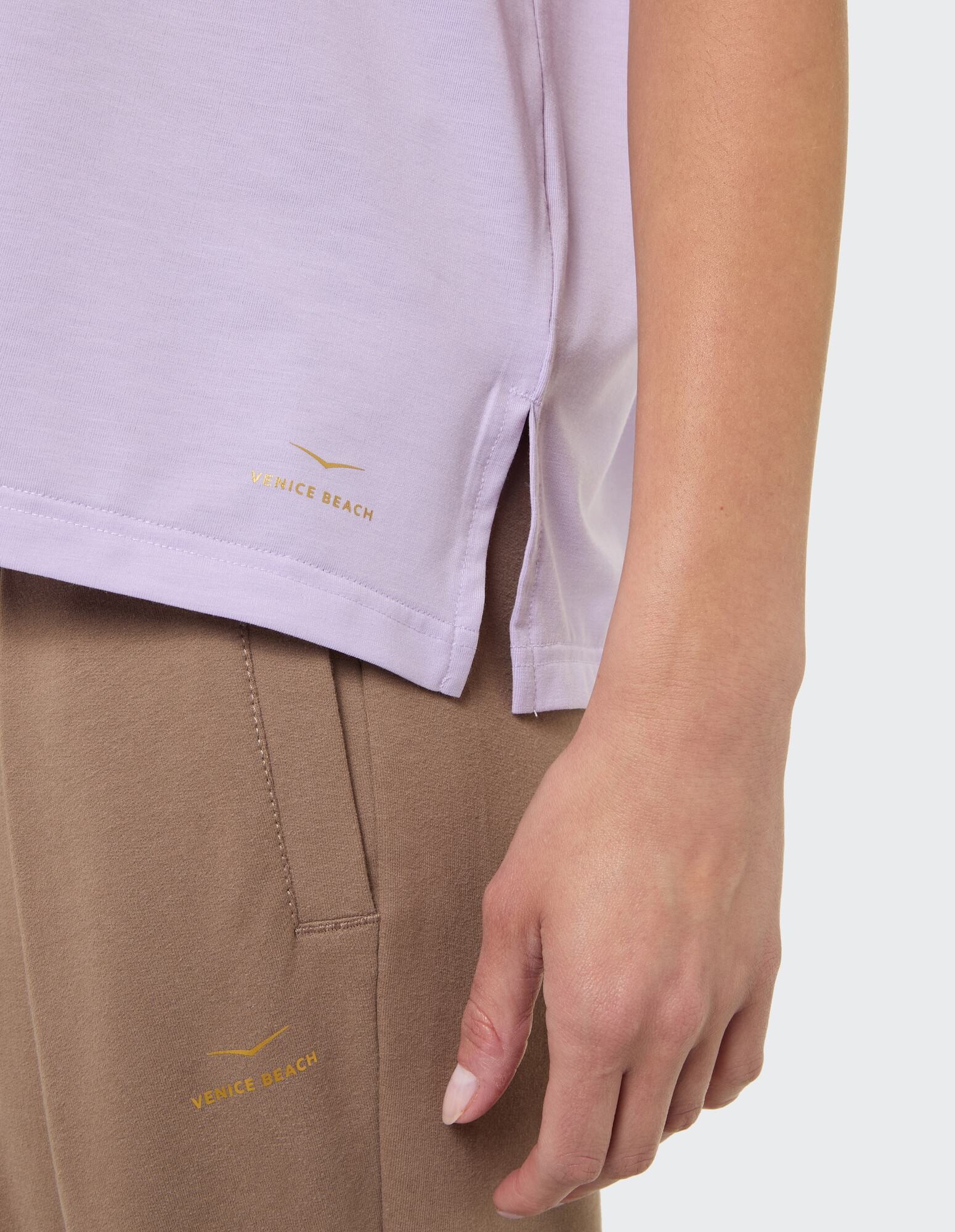 Nahaufnahme eines fliederfarbenen Oberteils mit Seitenschlitzen und einer beigen Hose mit Venice Beach-Branding.