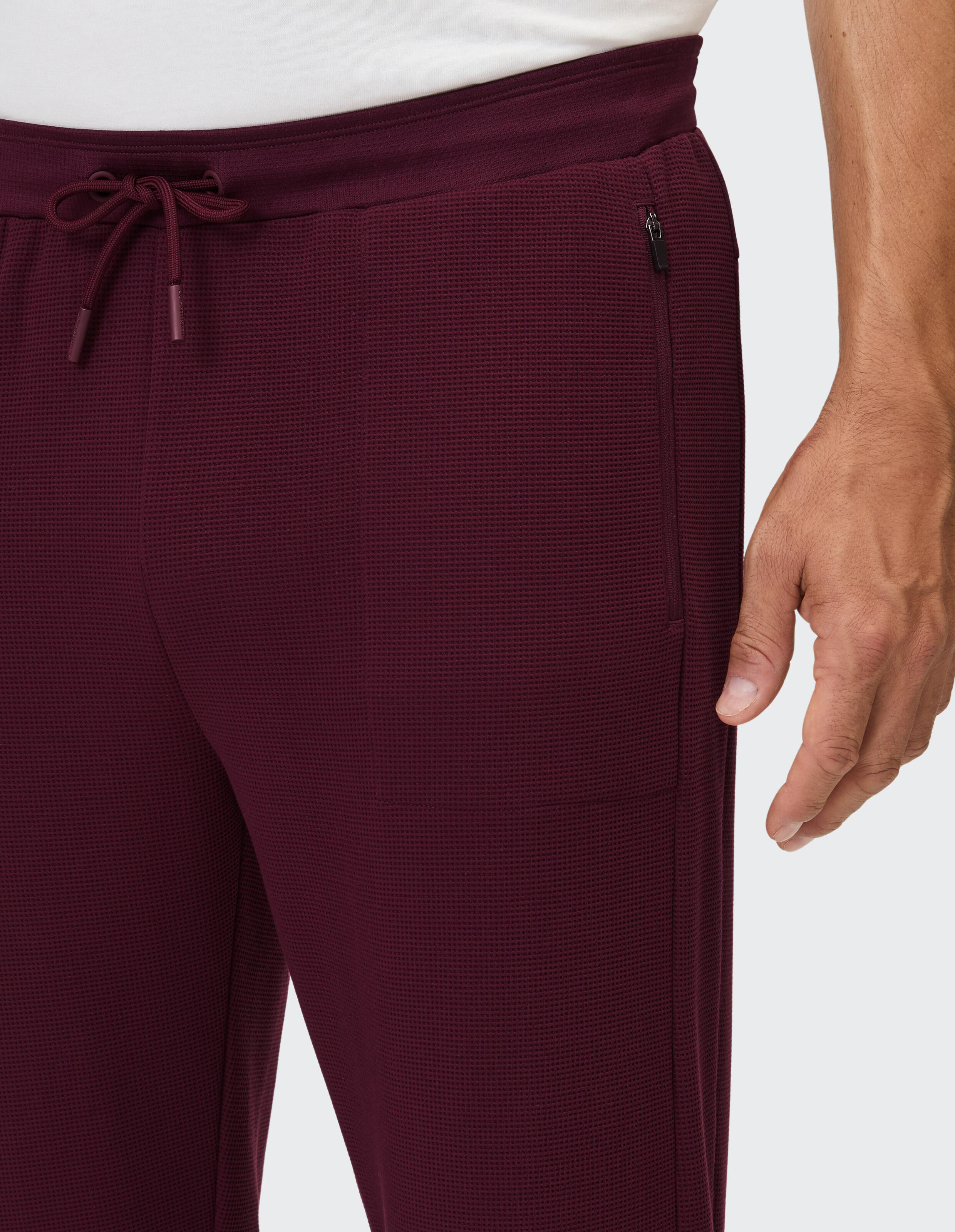 Nahaufnahme einer burgunderroten Freizeithose mit strukturiertem Stoff und Seitentasche.
