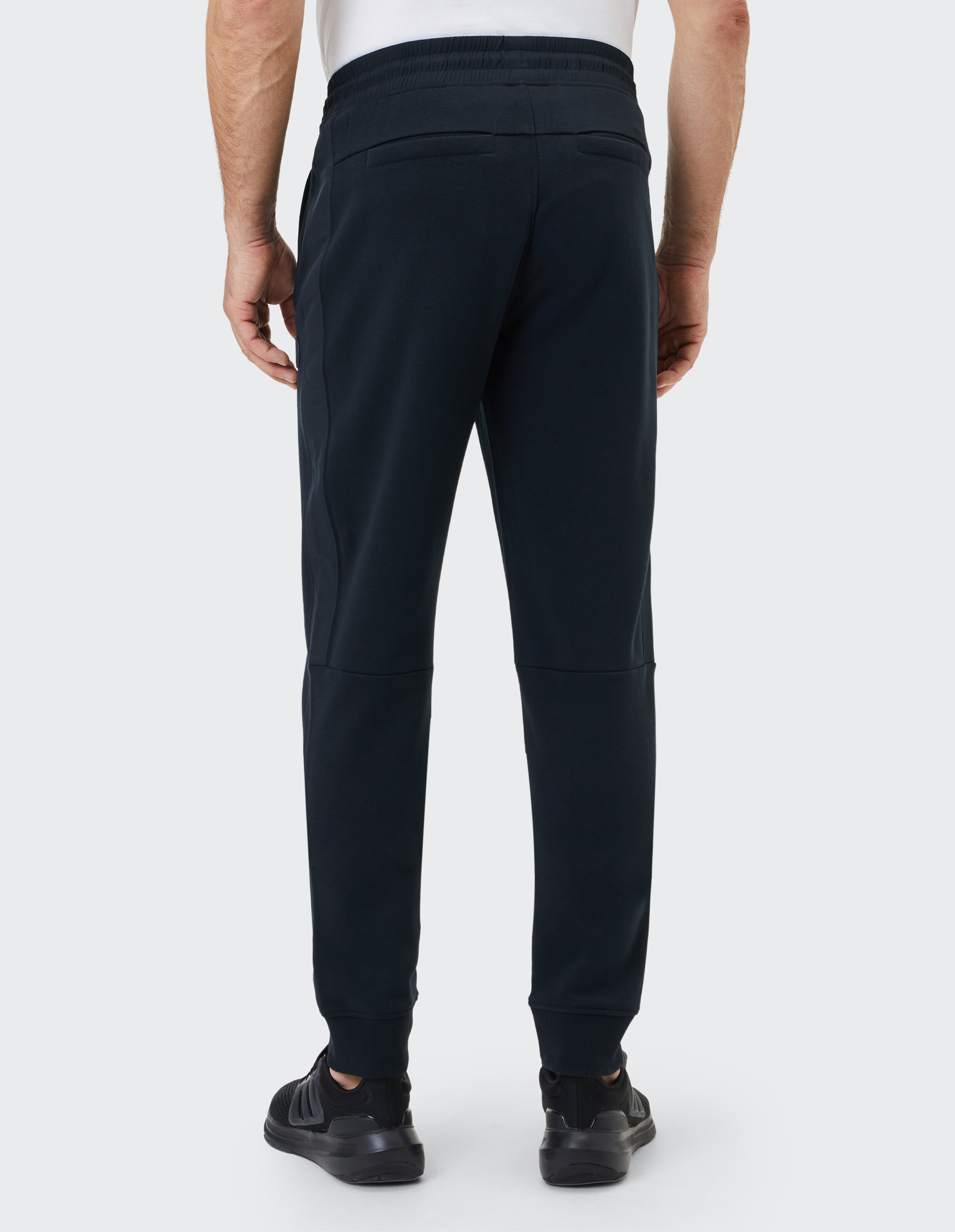 Rückansicht eines Mannes, der dunkelblaue Freizeitjogginghosen und schwarze Turnschuhe trägt.