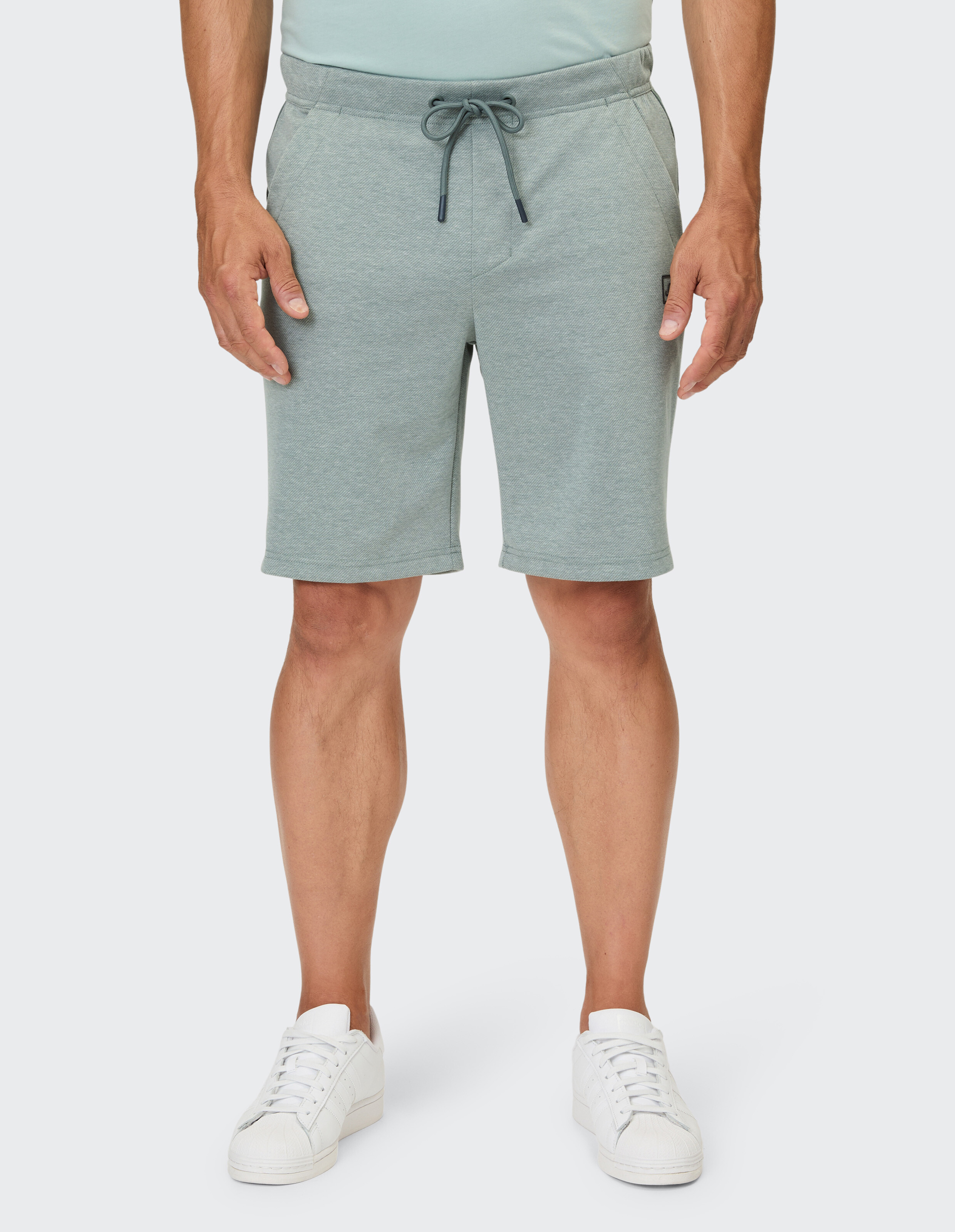 Ein Mann trägt eine hellgrüne, knielange Shorts mit einem Kordelzug am Bund.