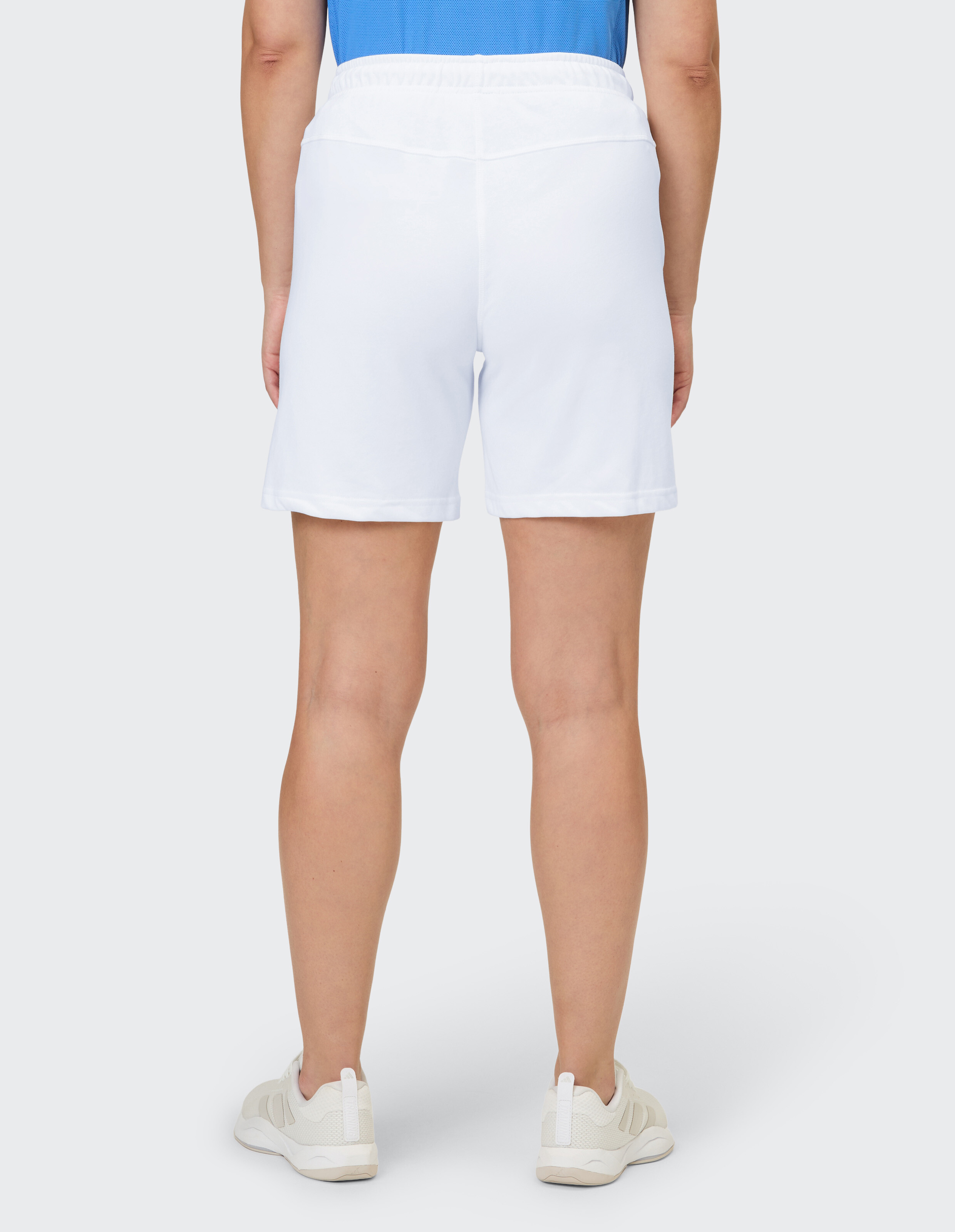 Eine Person trägt weiße, knielange Shorts mit einem Gummizug in der Taille und dazu passende Turnschuhe.