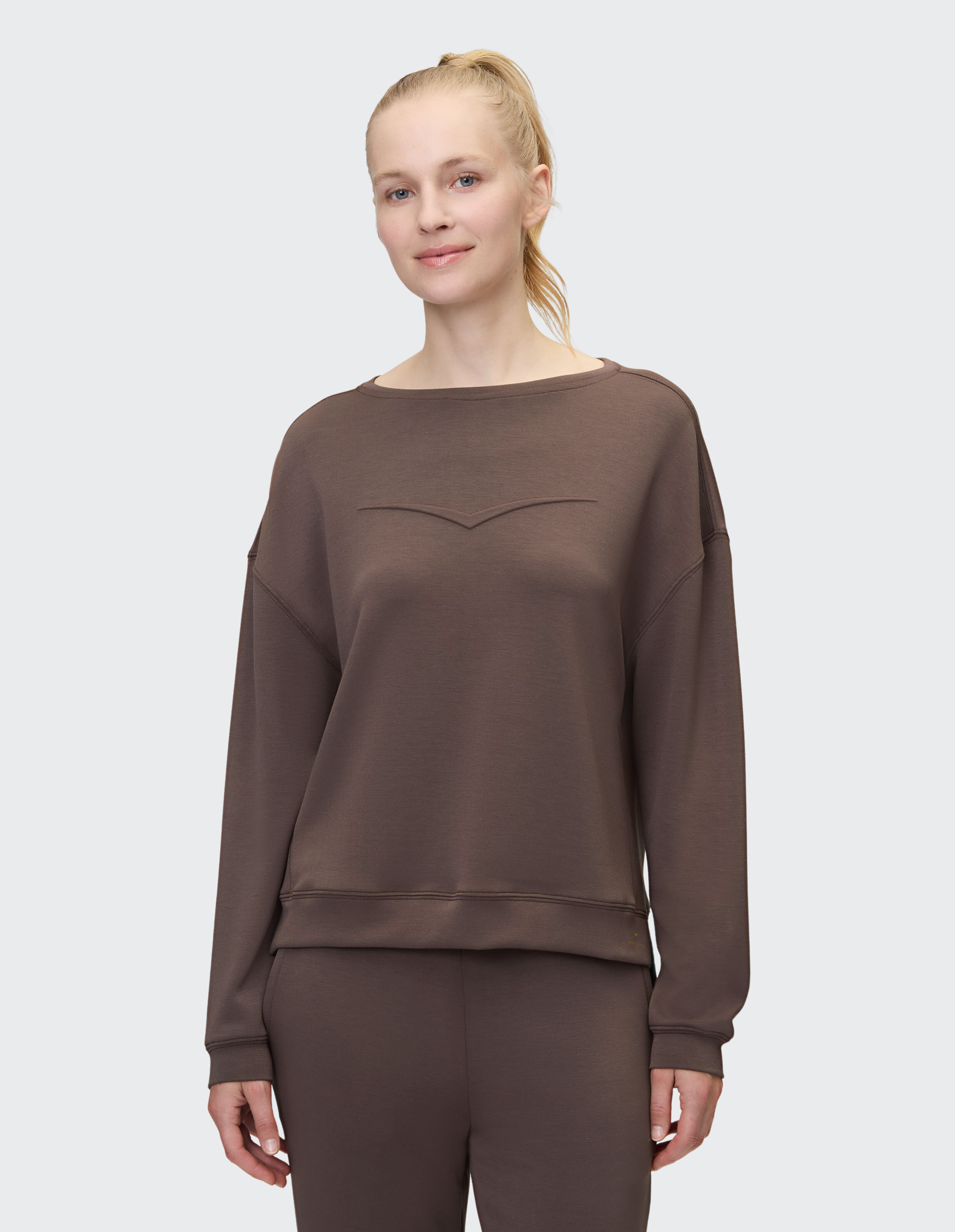 Frau trägt ein gemütliches dunkelbraunes Langarm-Sweatshirt zum entspannten Faulenzen.