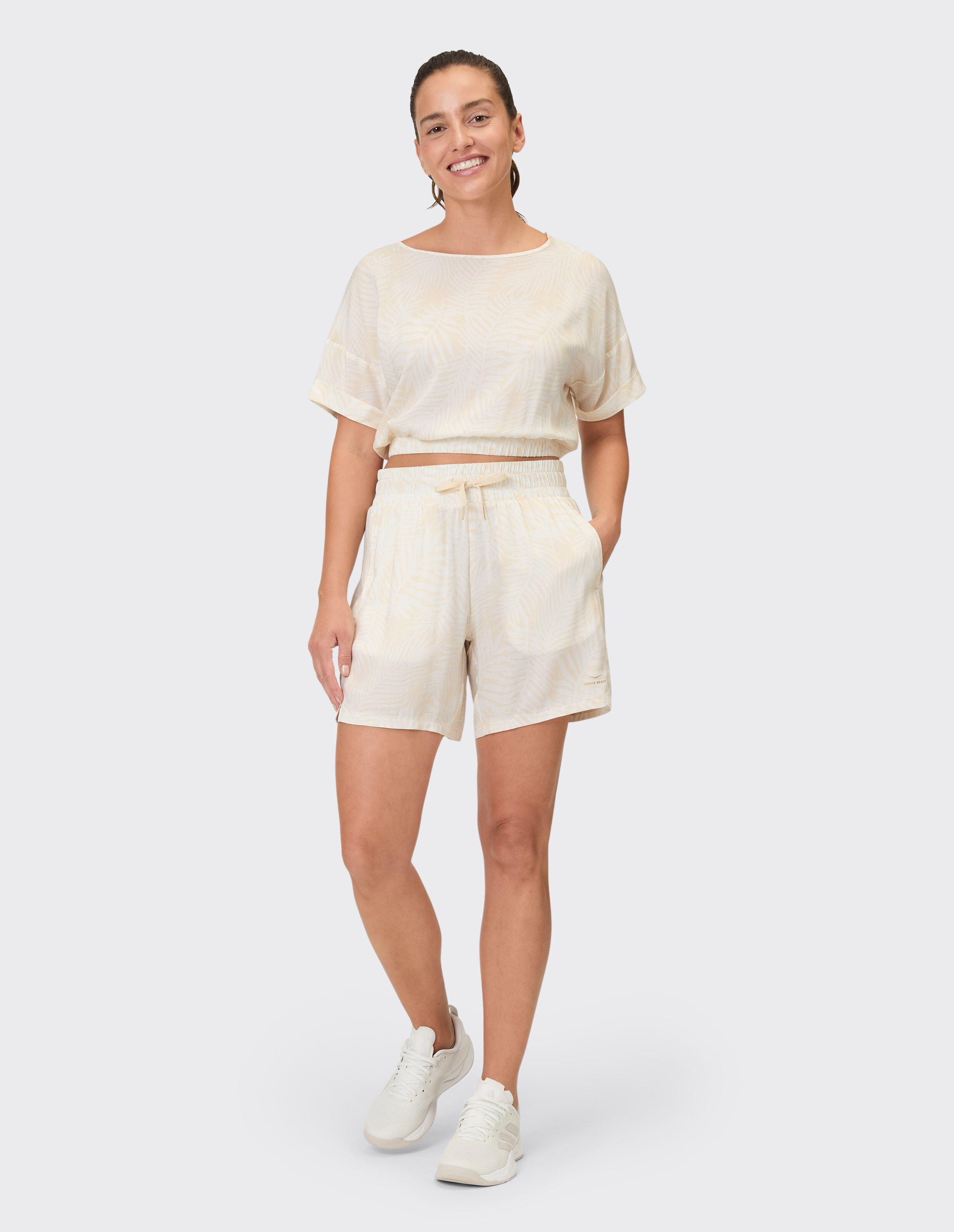 Frau trägt ein beige gemustertes Lounge-Set mit einem kurzen Oberteil und Shorts.