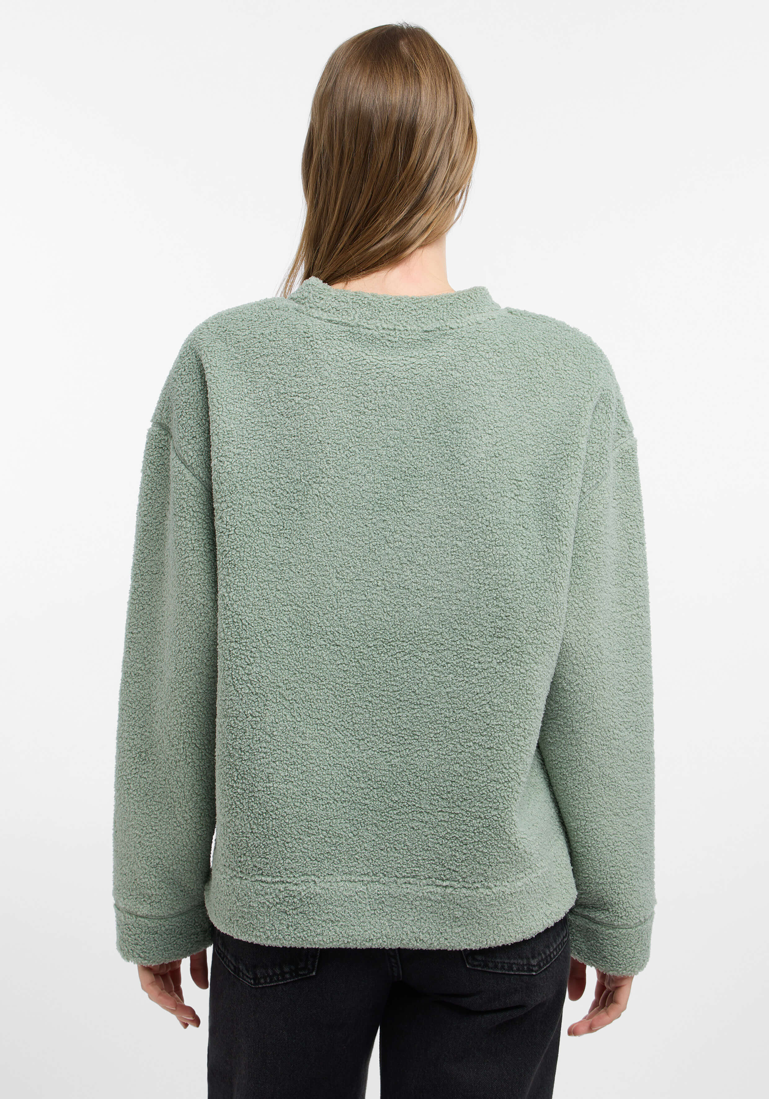 Rückansicht einer Frau, die einen kuscheligen salbeigrünen Teddyfleece-Pullover für einen lässigen Lounge-Stil trägt.