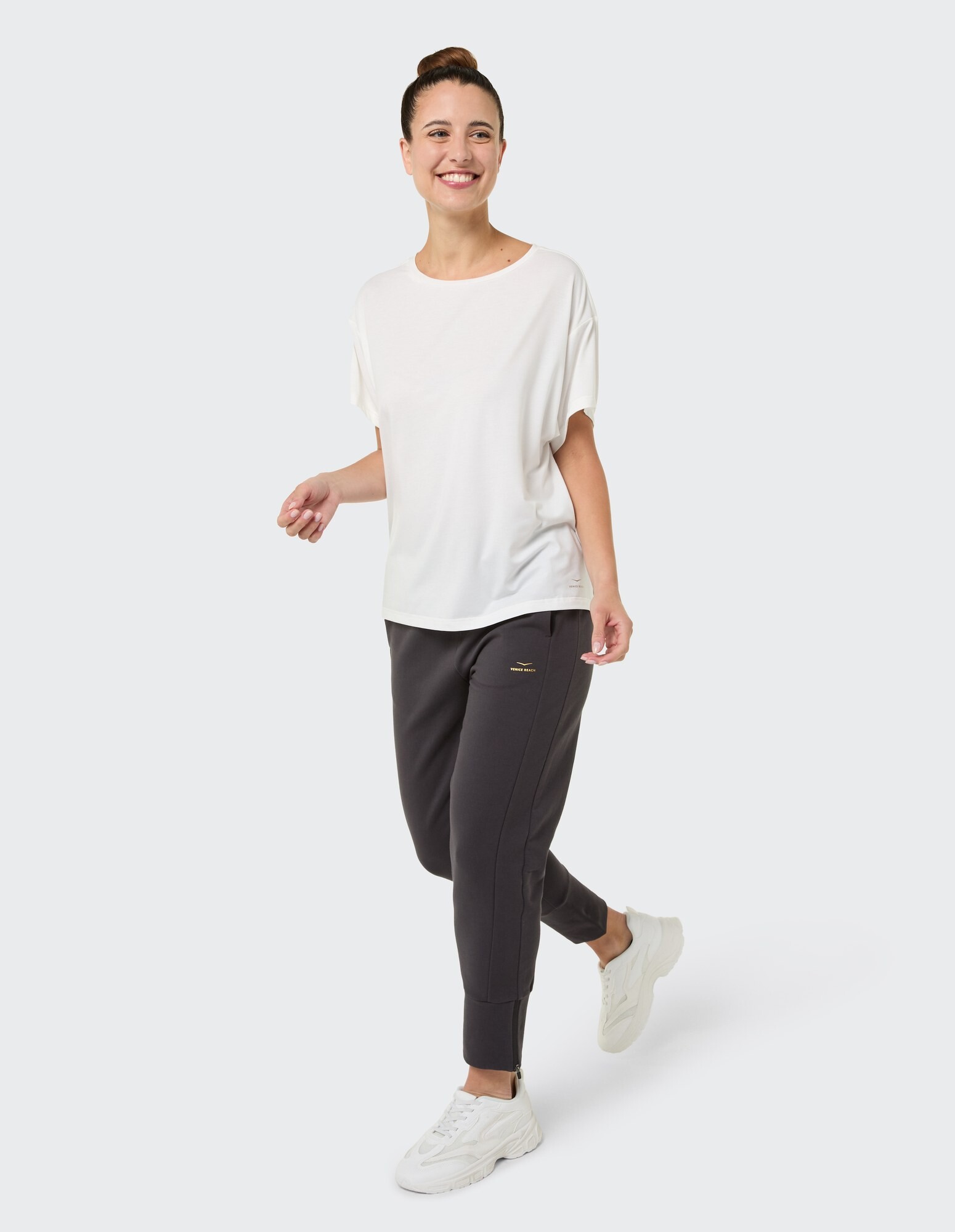 Frau in weißem, entspanntem T-Shirt und dunkler Jogginghose, stilvolle Freizeitkleidung.