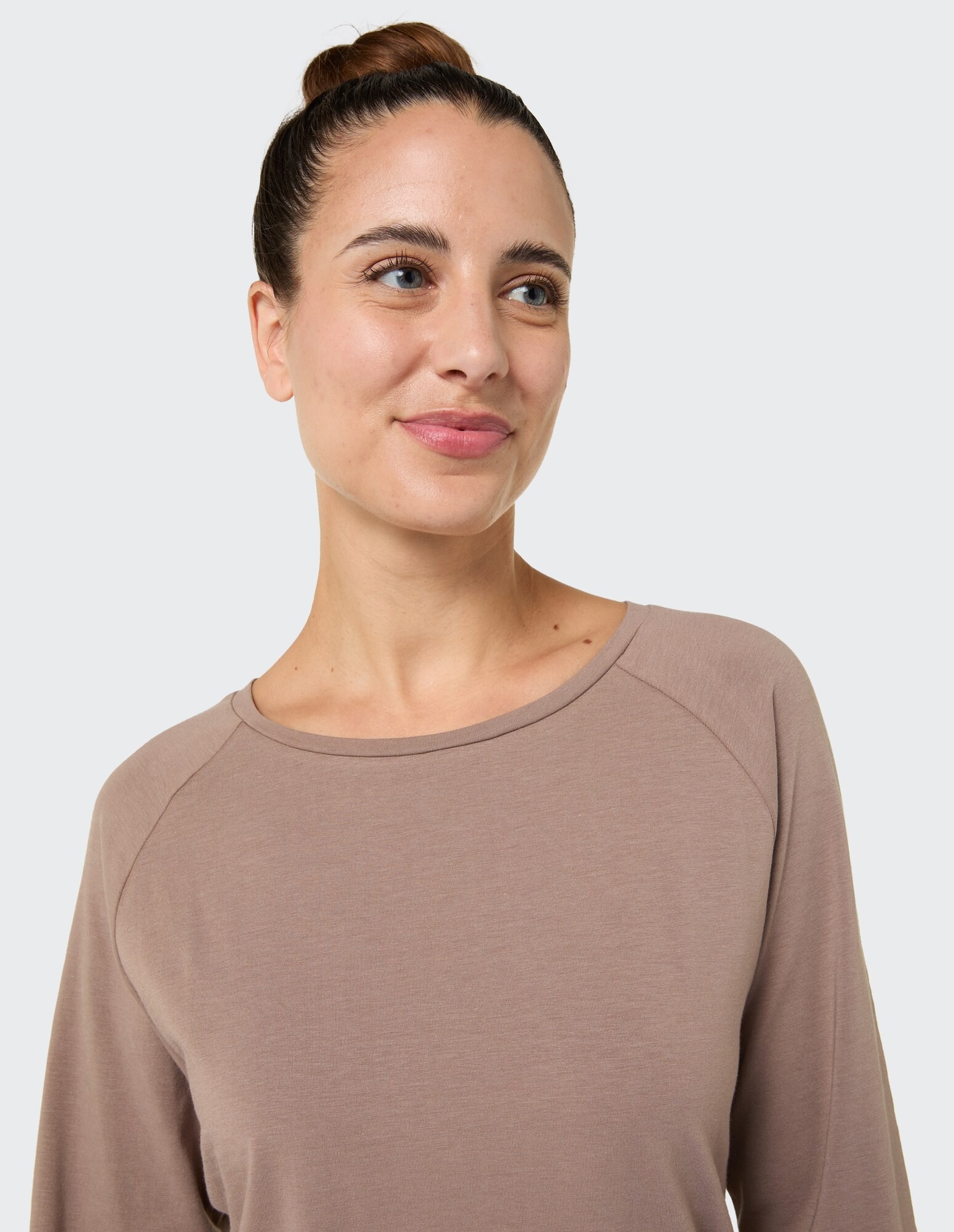 Nahaufnahme einer Frau in einem kuscheligen taupefarbenen Langarmshirt, die sanft lächelt.