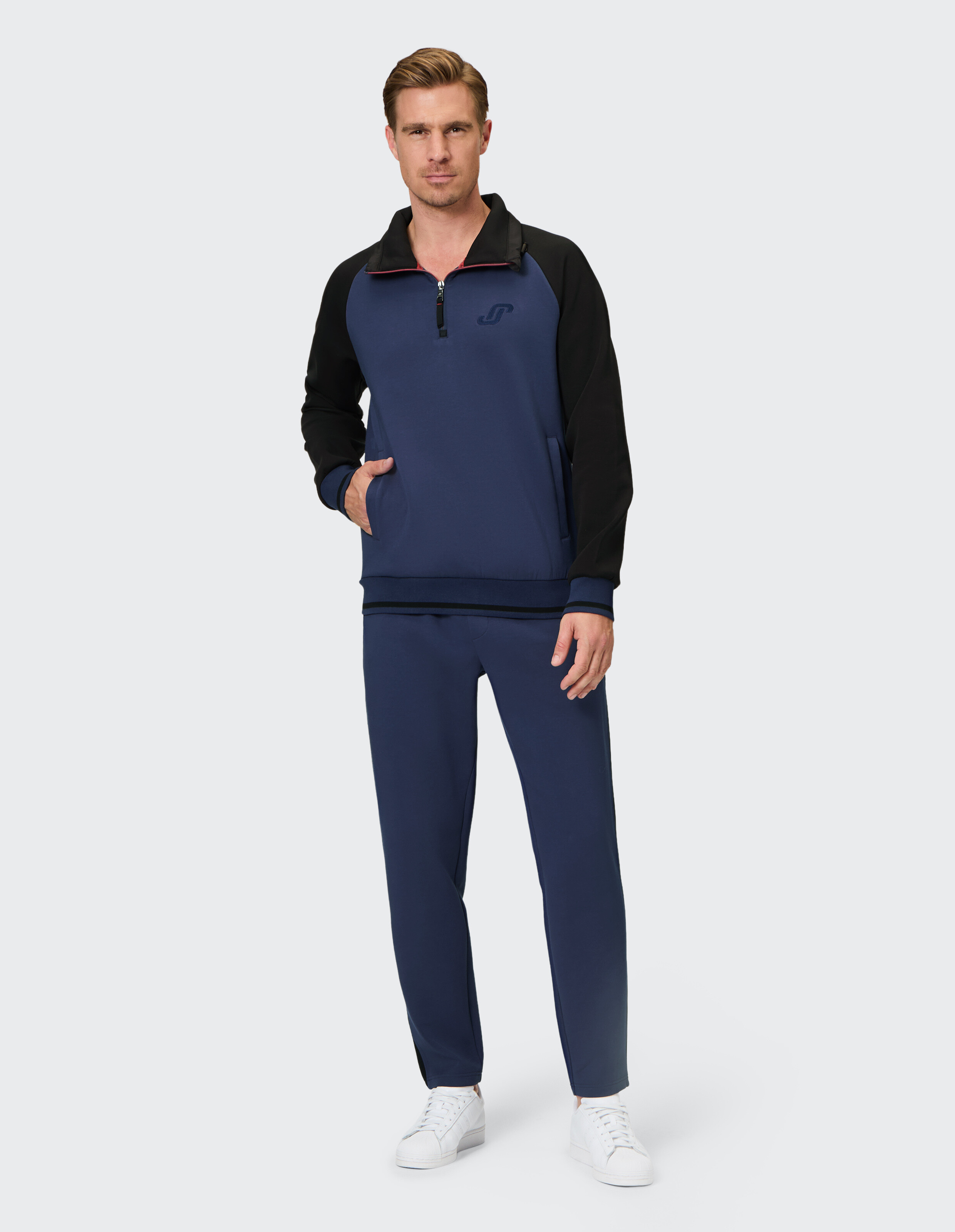Mann trägt ein blau-schwarzes Sweatshirt mit Viertelreißverschluss und passende Jogginghosen.