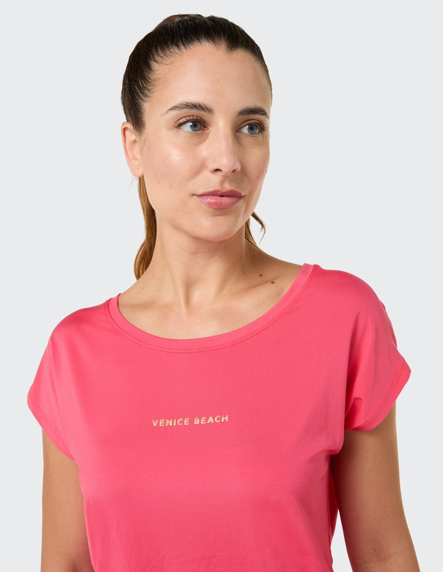 Frau trägt ein rosafarbenes Freizeit-T-Shirt mit dem Aufdruck „Venice Beach“ in Gold.