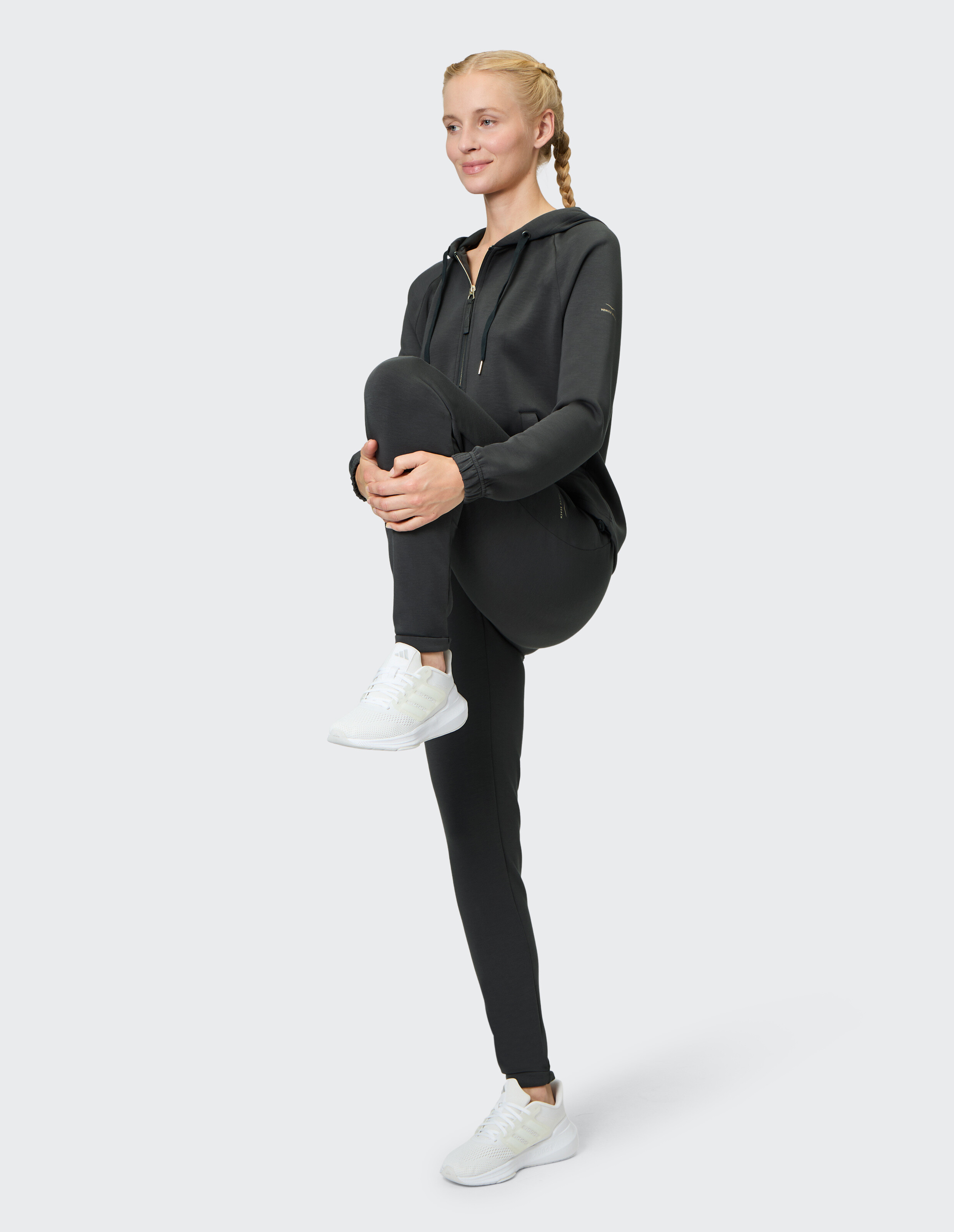 Frau in schwarzem Kapuzenpullover und Leggings präsentiert bequeme Freizeitkleidung für einen aktiven Lebensstil.