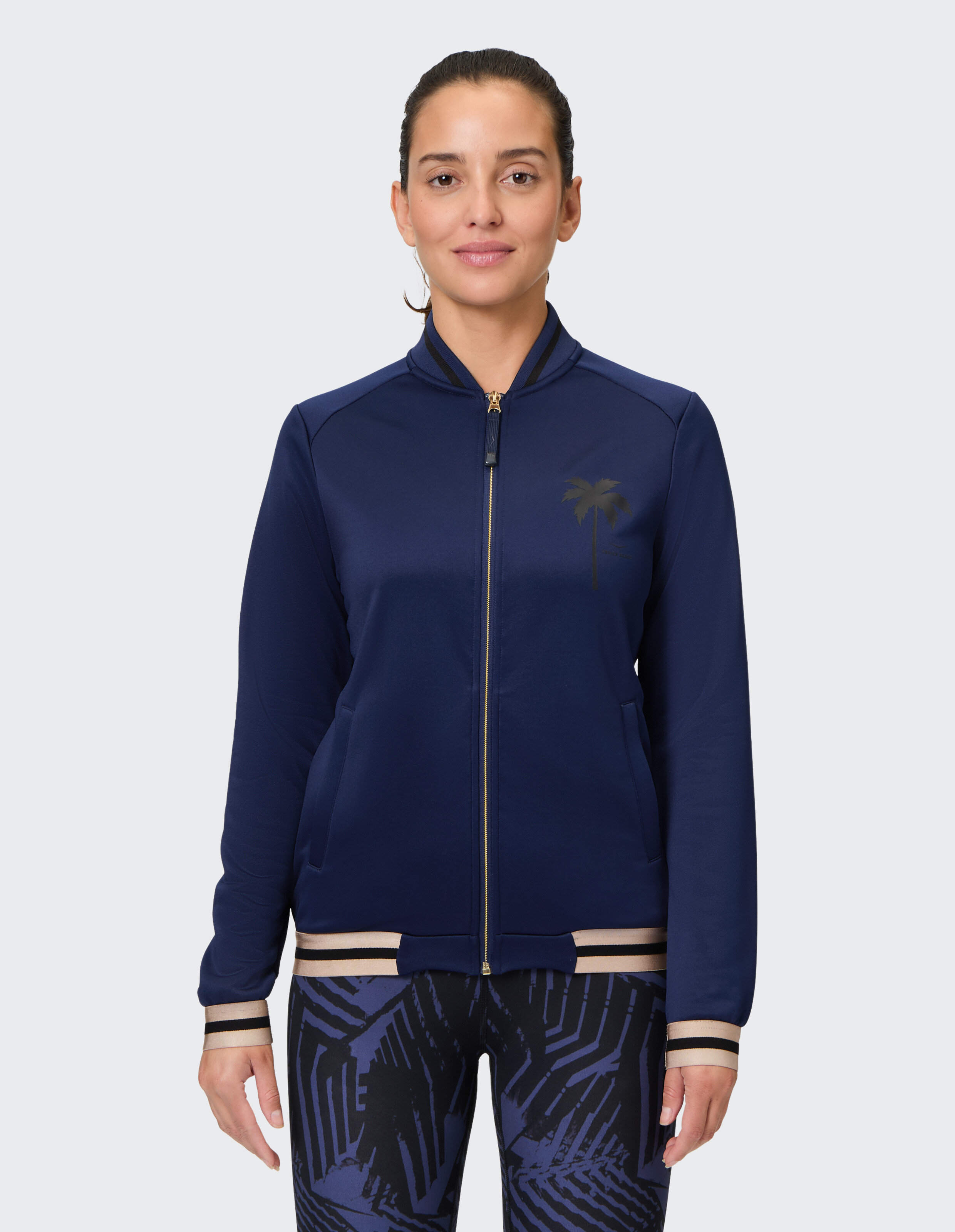 Marineblaue Jacke mit Reißverschluss und Palmenmuster, gepaart mit gemusterten Leggings.