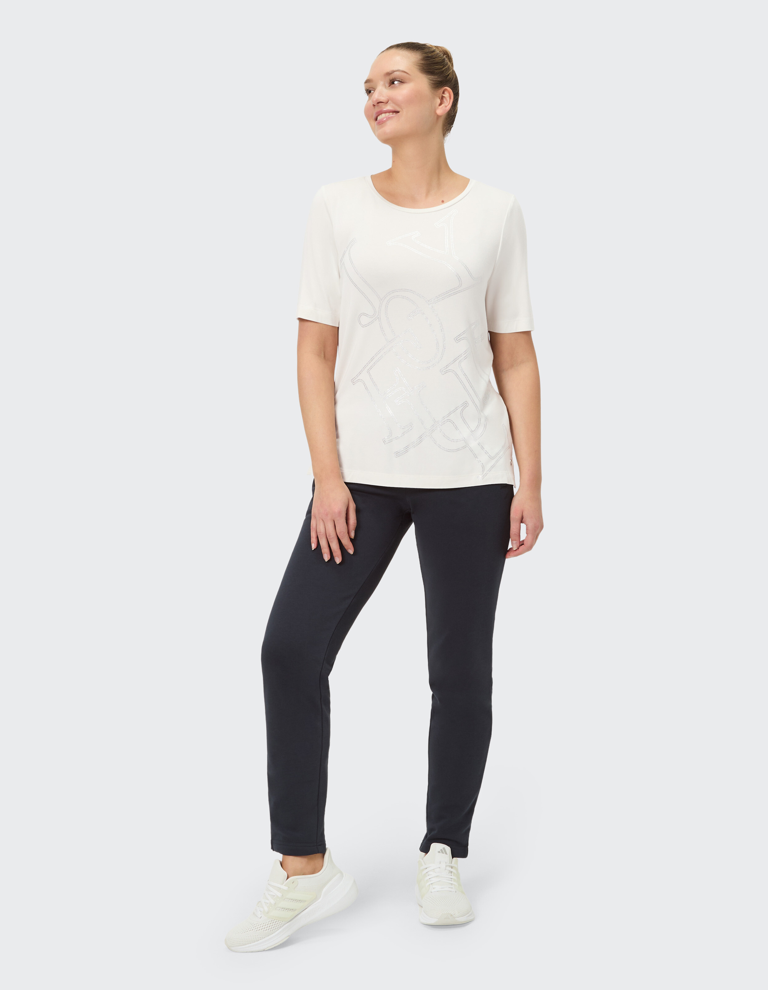 Frau in einem weißen Grafik-T-Shirt und einer dunklen Hose, gestylt für lässigen Komfort.