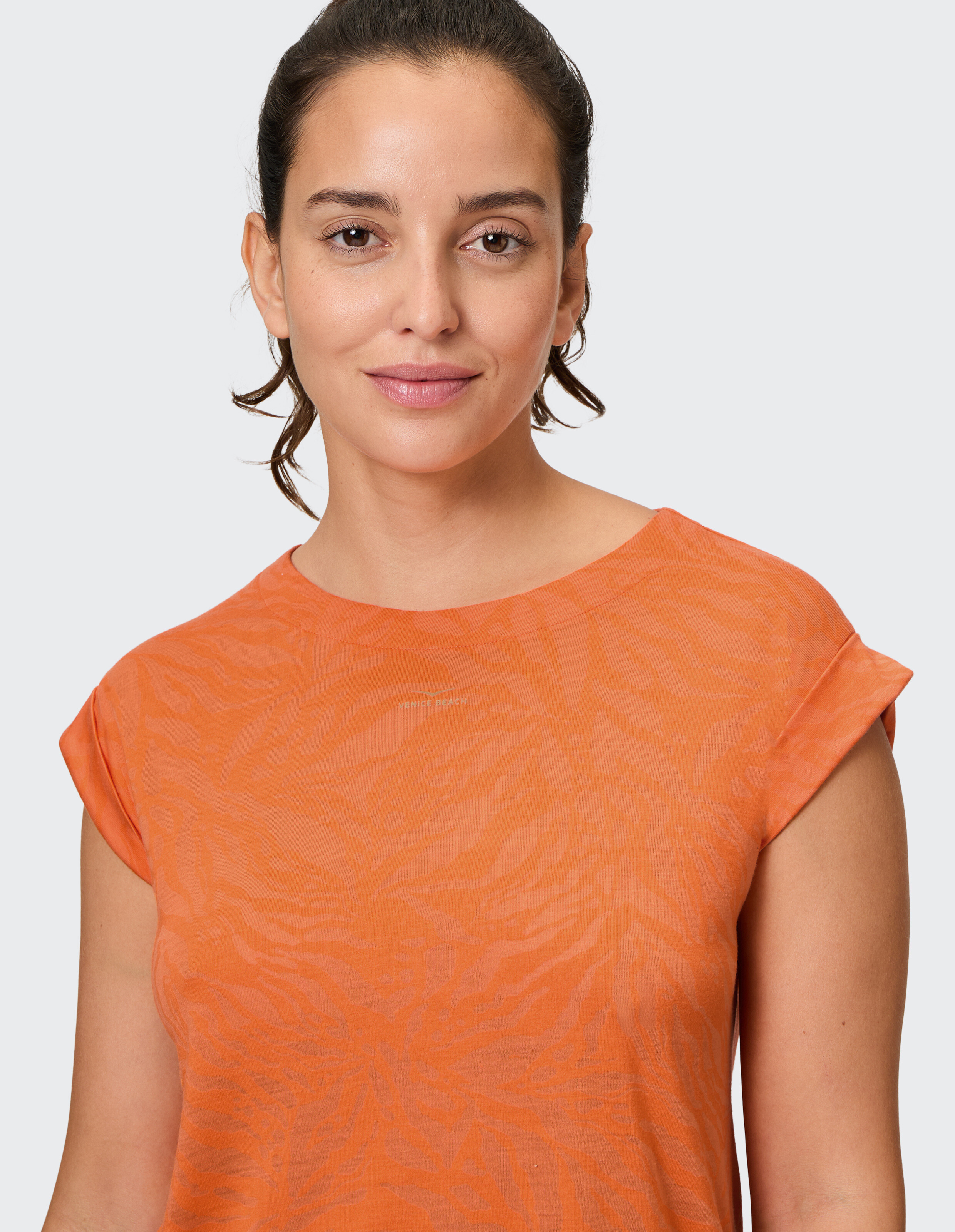 Frau trägt ein gemütliches orangefarbenes Freizeit-T-Shirt mit einem dezenten, farblich abgestimmten Animal-Print-Muster.