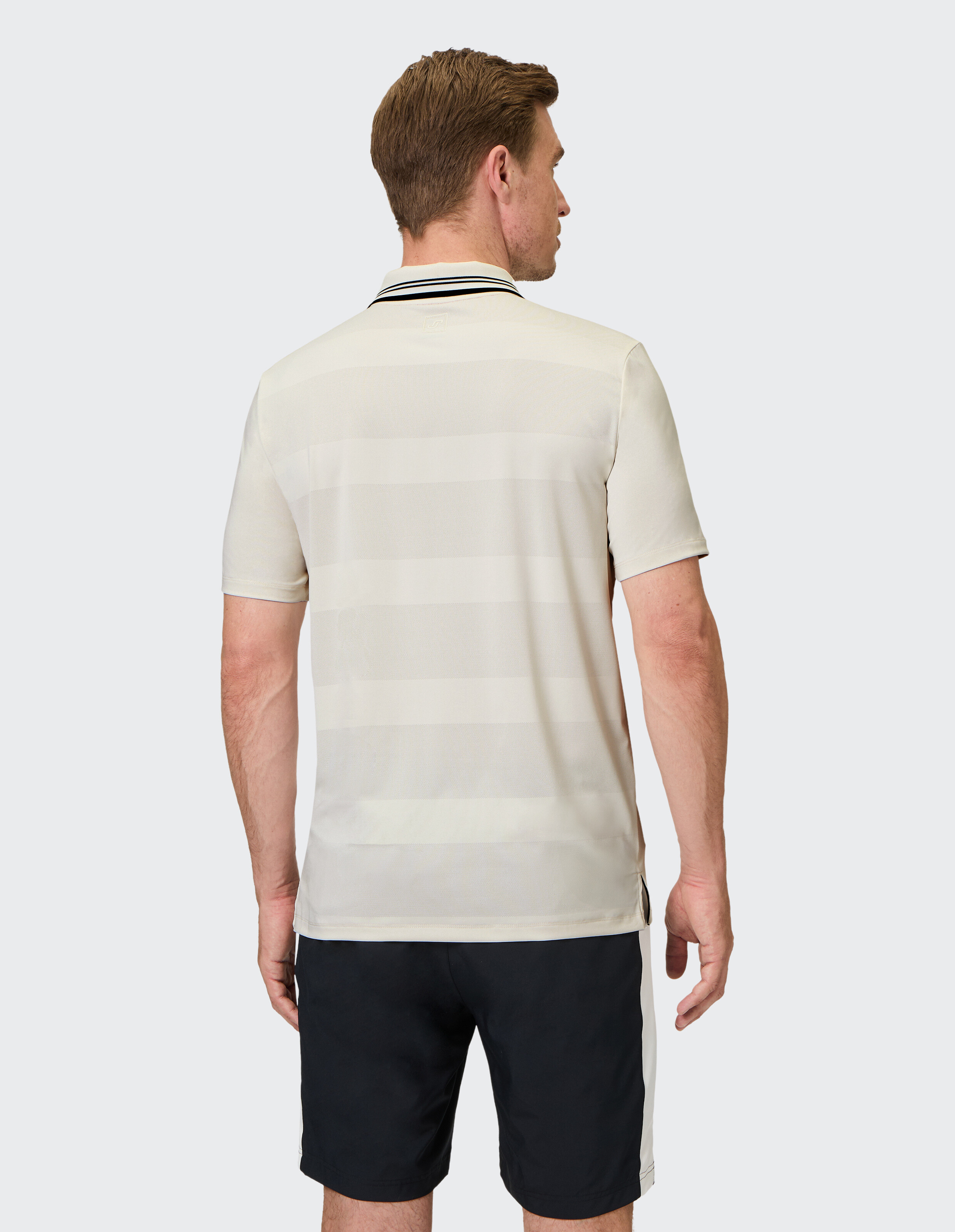 Rückansicht eines Mannes in einem hell gestreiften Poloshirt und dunklen Shorts.