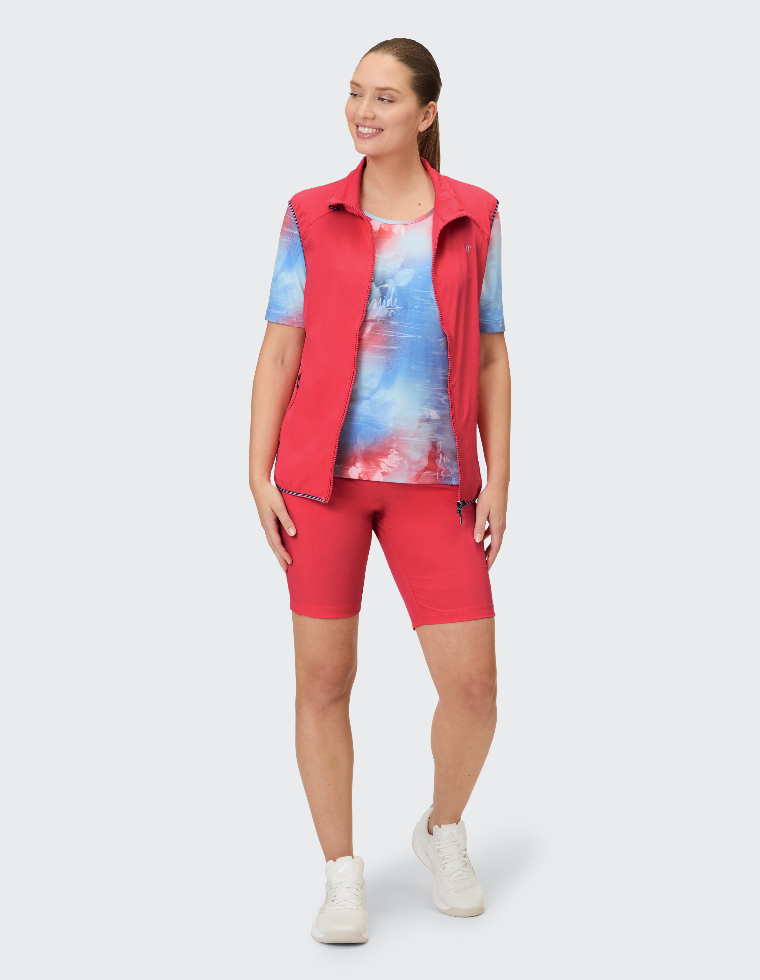Frau in roter Weste und passenden Shorts, trägt ein farbenfrohes Batik-Oberteil.