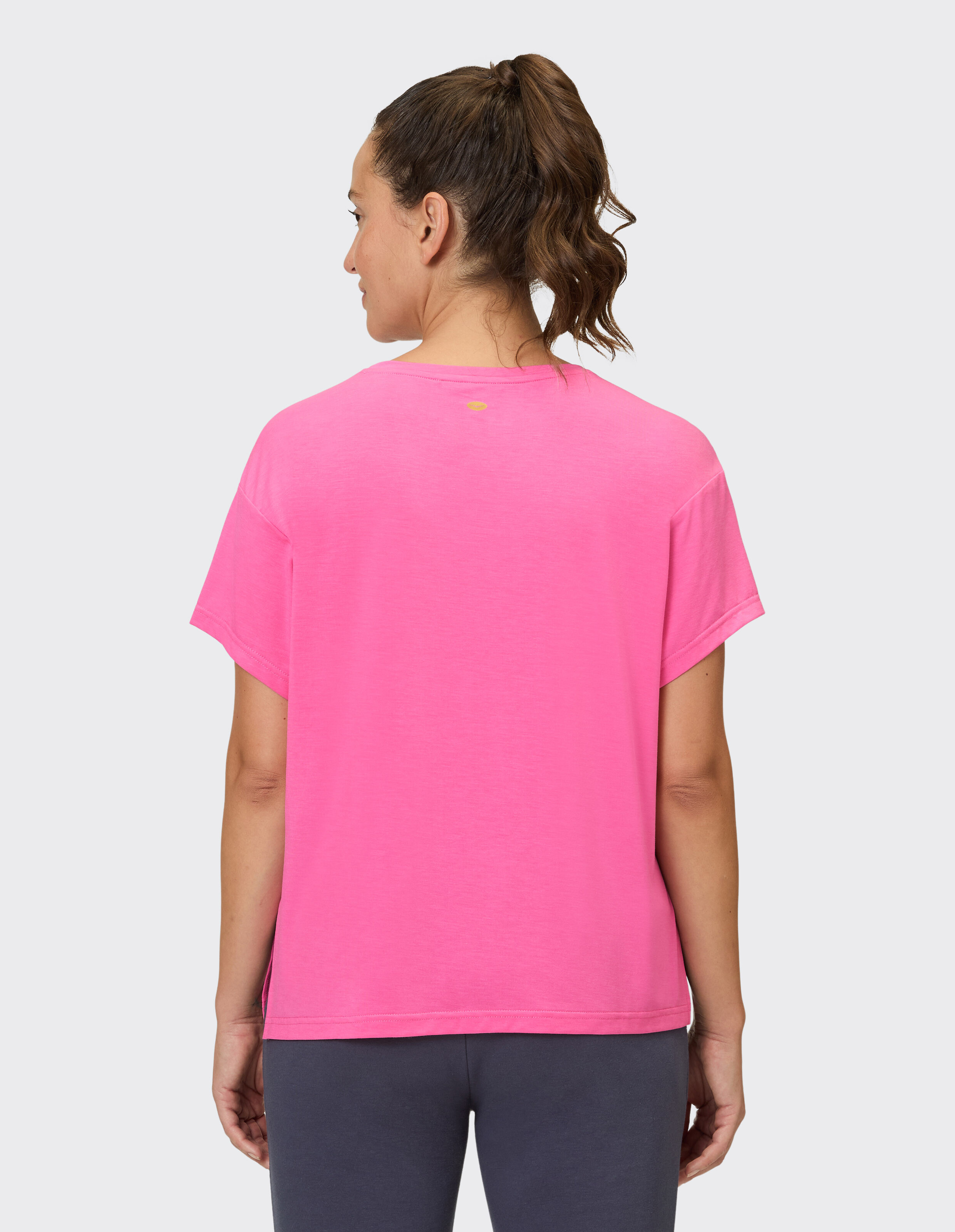 Rückansicht einer Frau, die ein leuchtend rosa Freizeit-T-Shirt mit kurzen Ärmeln trägt.