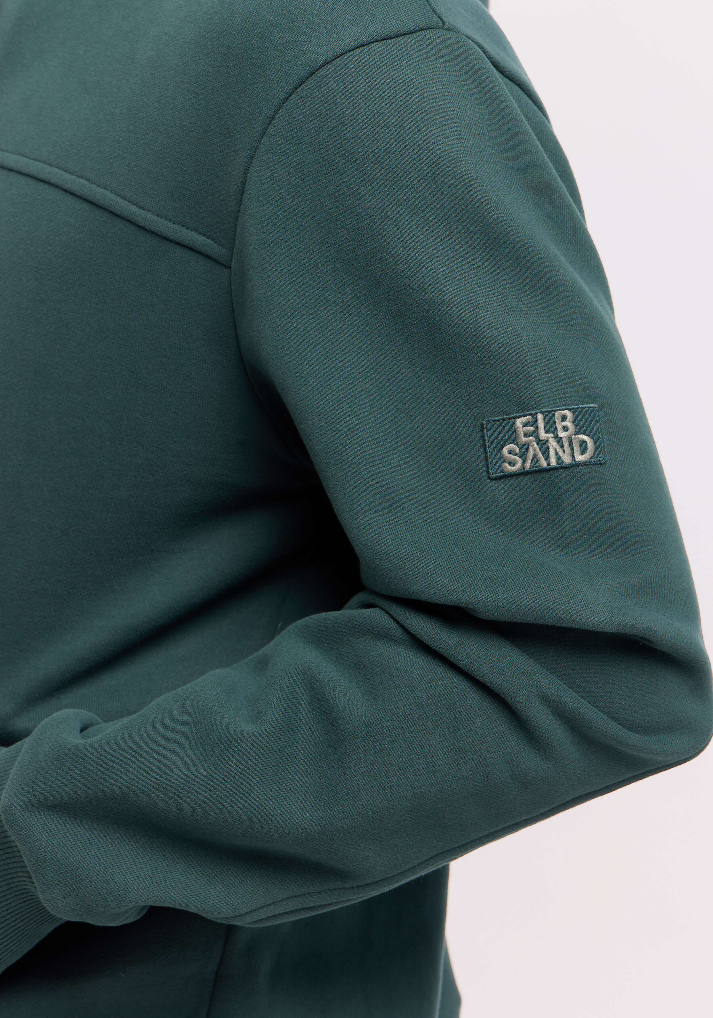 Nahaufnahme eines dunkelgrünen ELBSAND-Freizeit-Sweatshirtärmels mit Markenaufnäher.