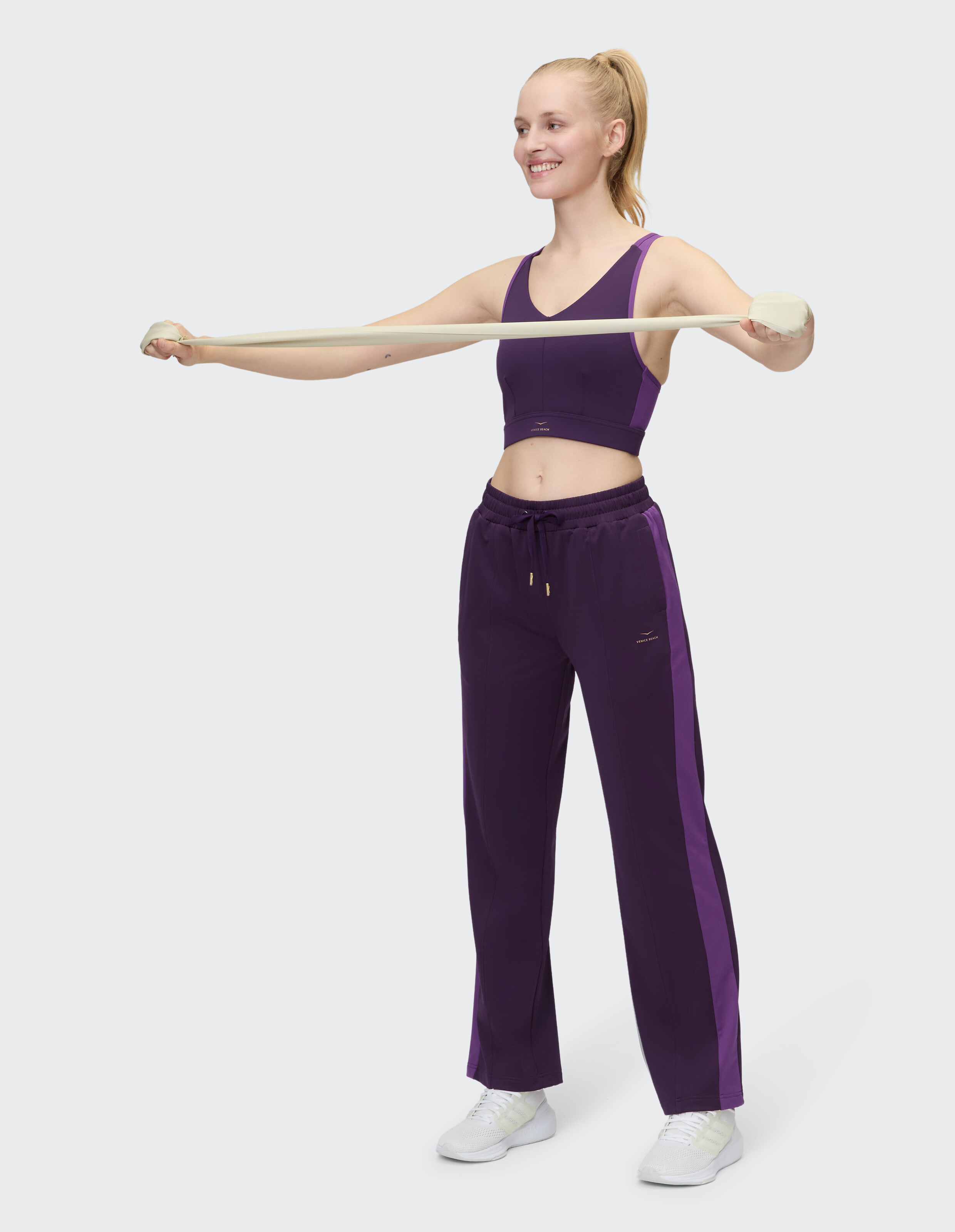 Frau in lila Sport-BH und passender Hose dehnt sich mit einem Widerstandsband.