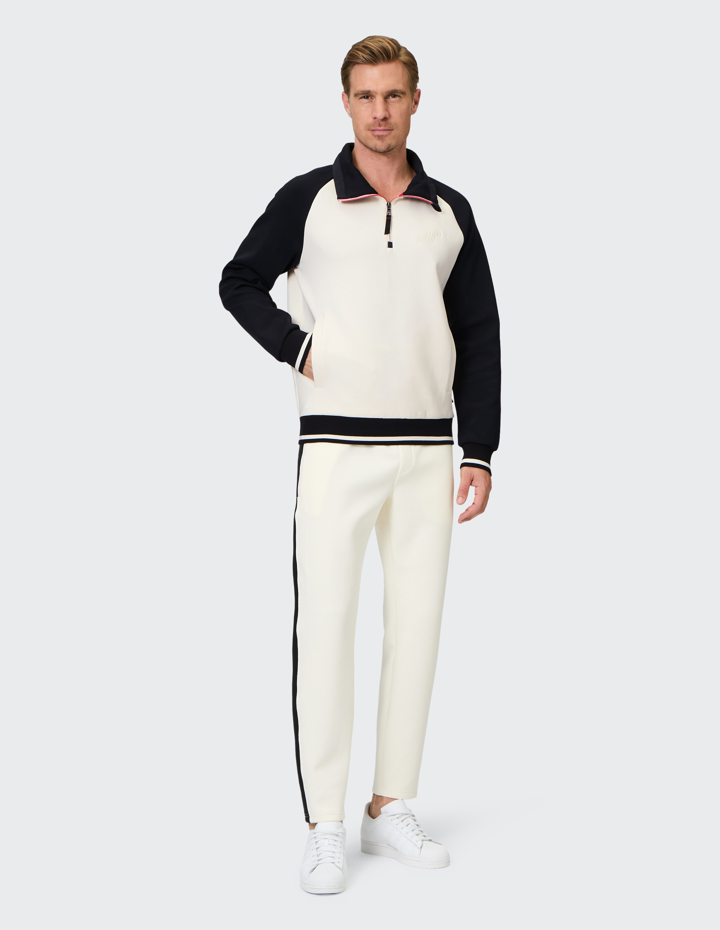 Mann trägt ein cremefarbenes und schwarzes Sweatshirt mit Viertelreißverschluss und eine passende Freizeithose.