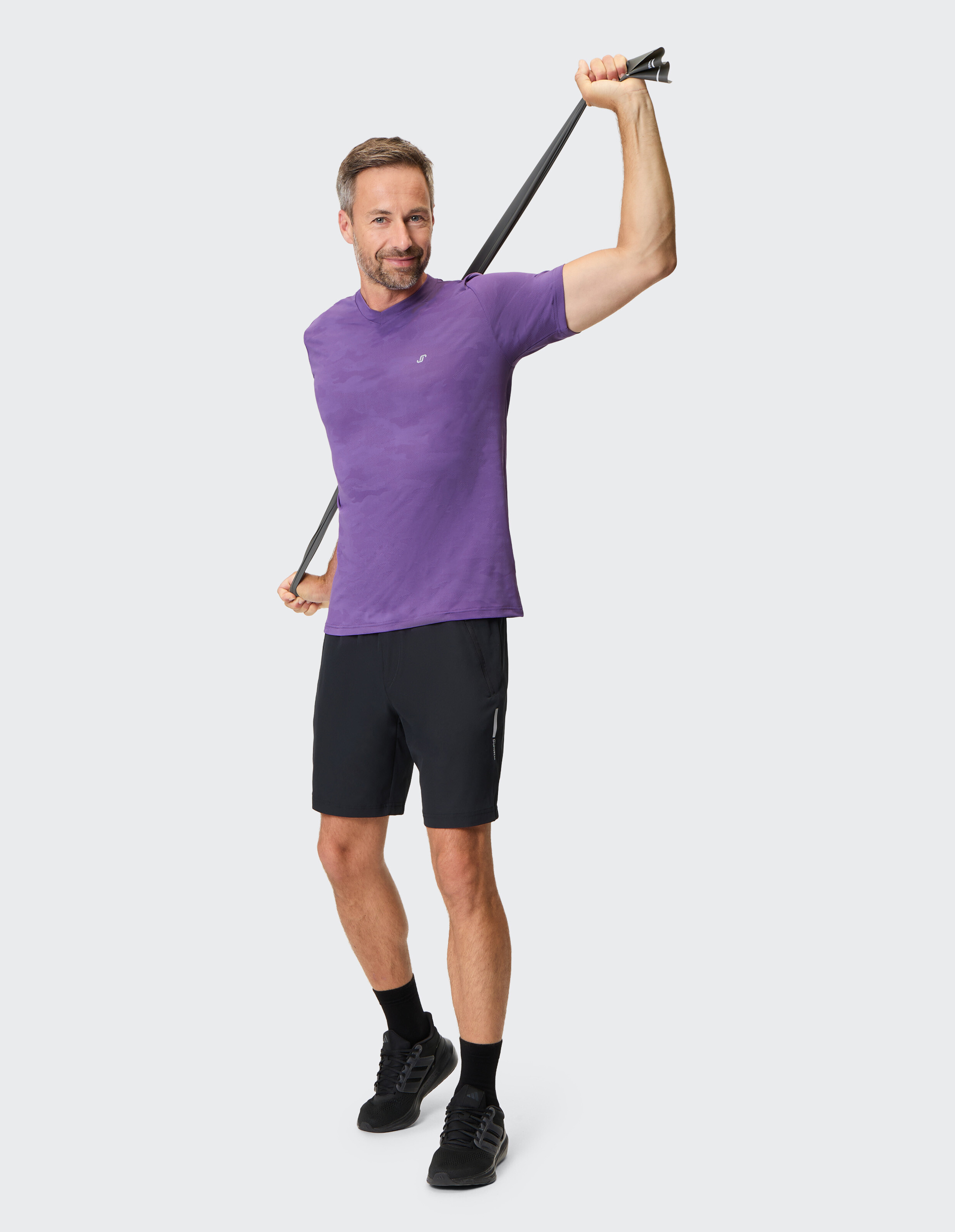 Mann in einem lila T-Shirt und schwarzen Shorts trainiert mit einem Widerstandsband.