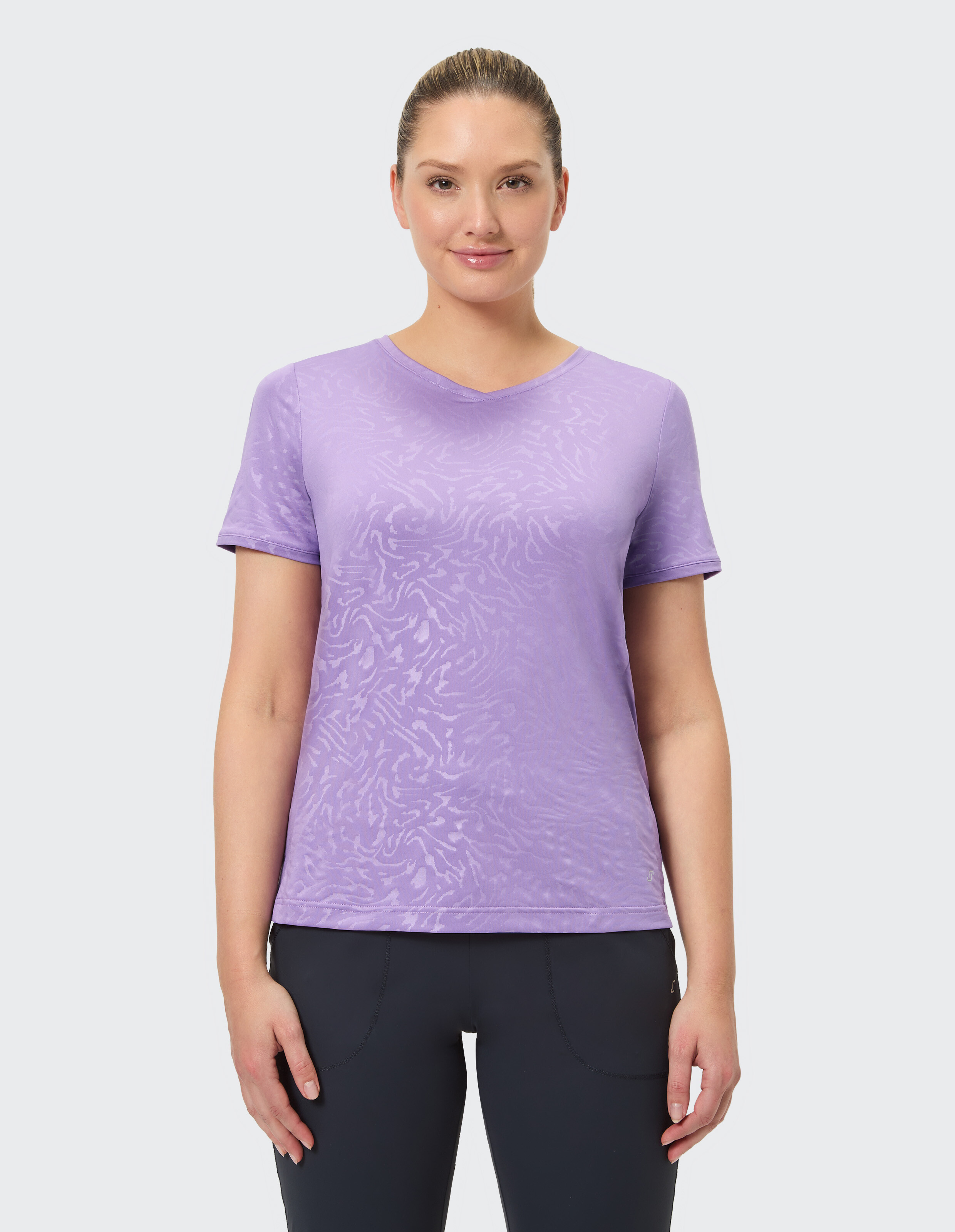 Frau trägt ein hellviolettes T-Shirt mit V-Ausschnitt und dezentem Muster, ideal für Freizeitkleidung.
