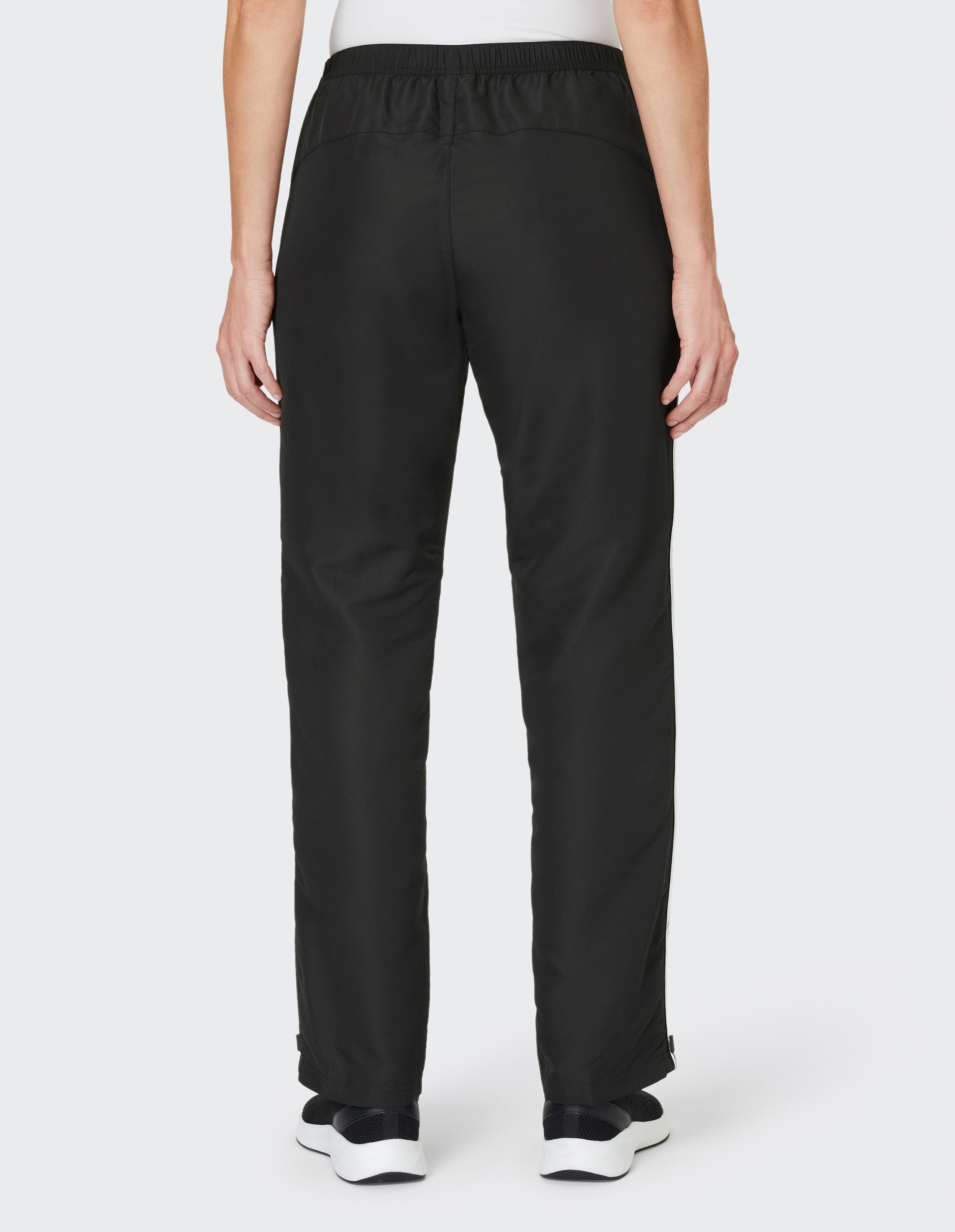 Person trägt schwarze, gerade geschnittene Hose mit elastischem Bund, von hinten gesehen, kombiniert mit sportlichen, schwarzen Sneakern.