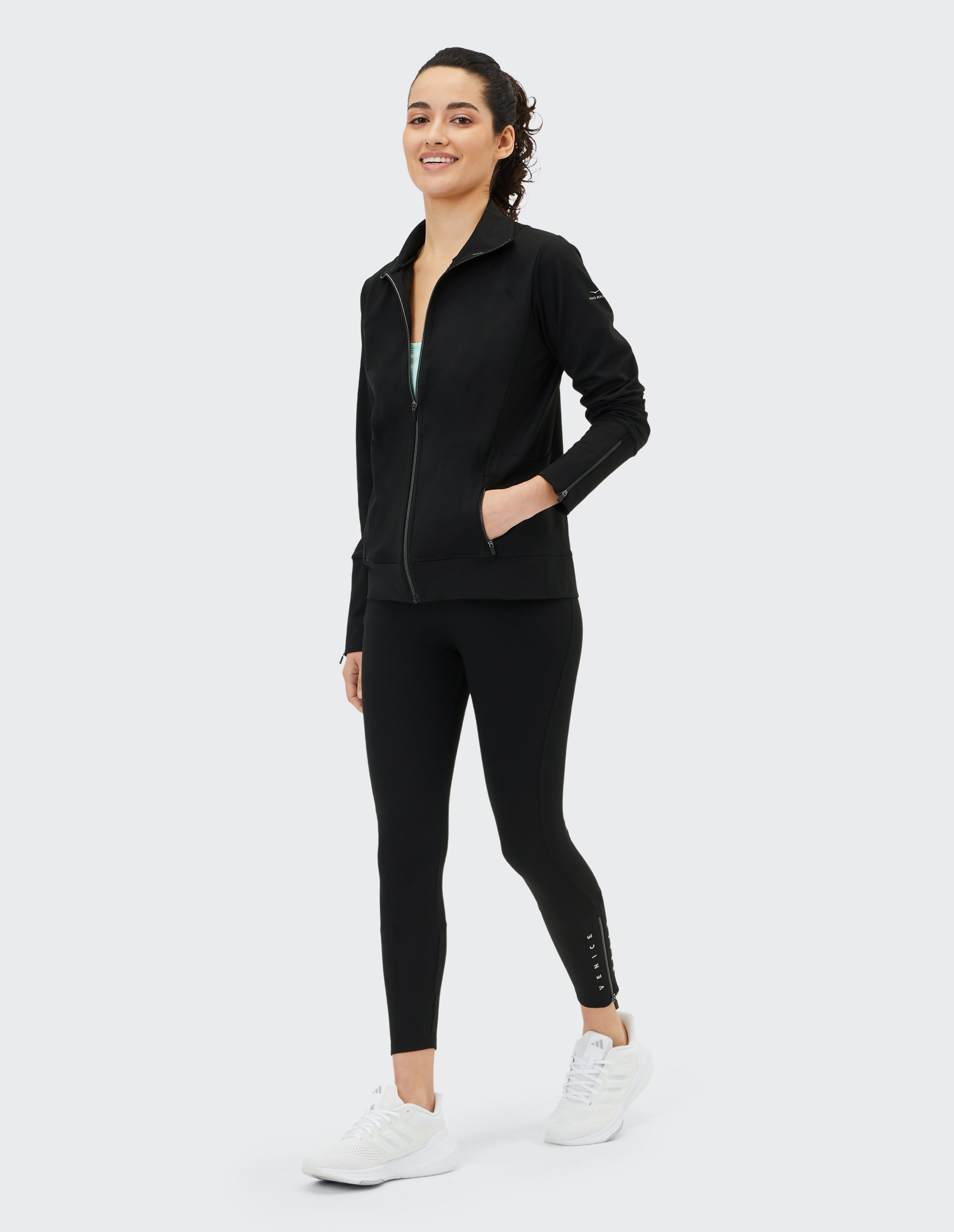 Frau trägt eine schwarze Sweatjacke von Venice Beach Caitria mit Reißverschluss und passende Leggings.
