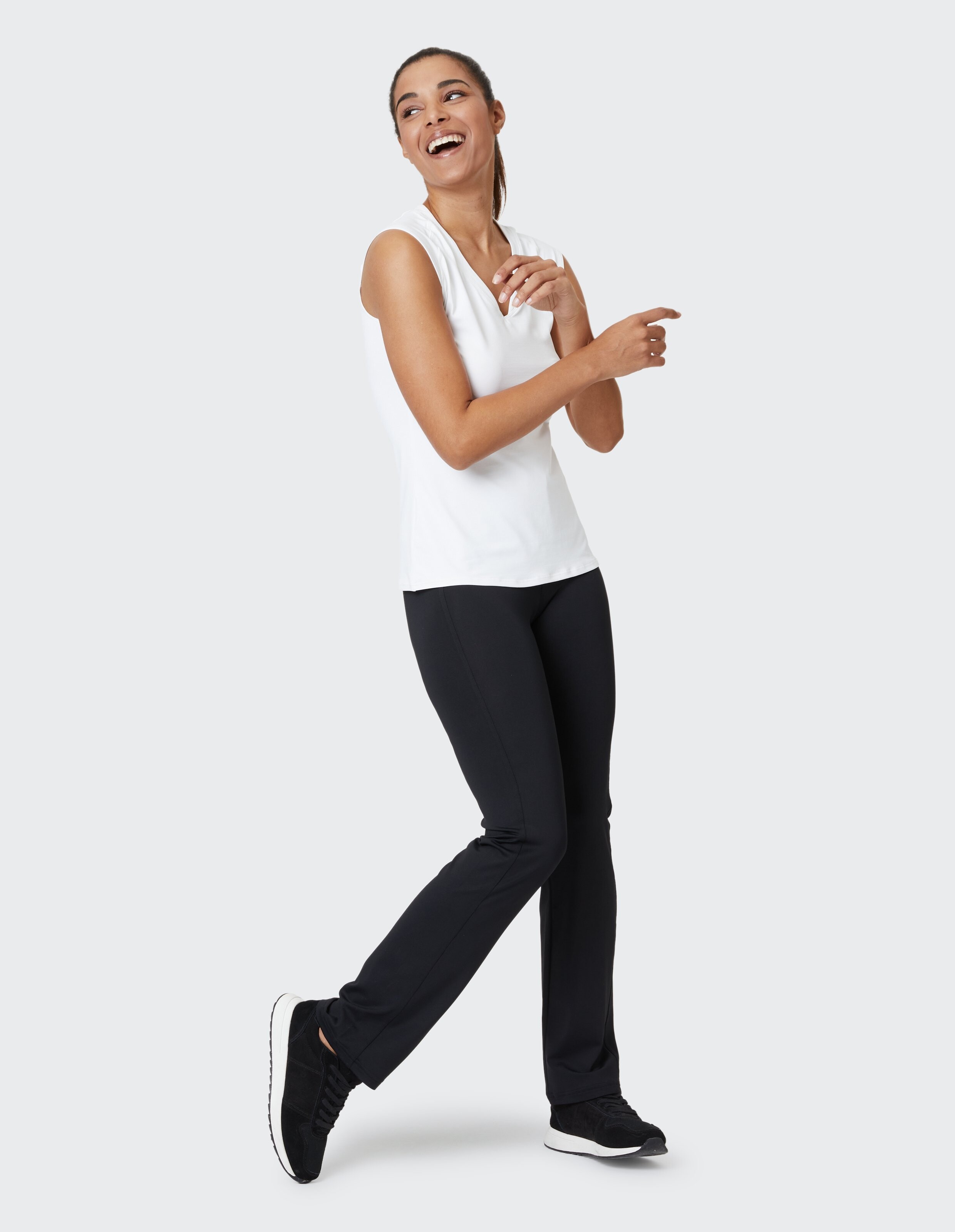 Frau trägt ein weißes ärmelloses Top und schwarze Leggings für einen gemütlichen, lässigen Look.