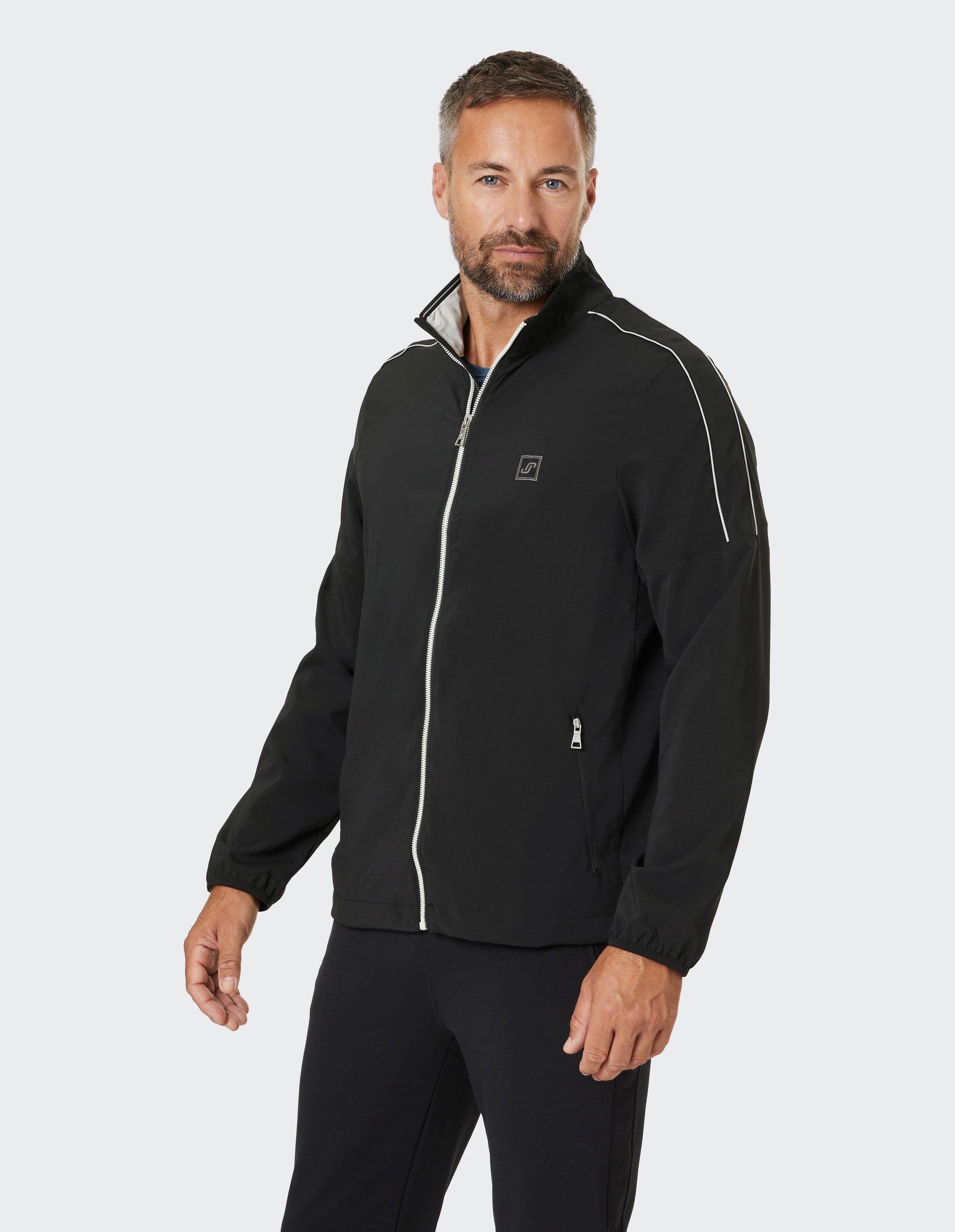 Eine schwarze Jacke mit weißem Reißverschluss und Paspeln, hohem Kragen und zwei Taschen mit Reißverschluss auf der Vorderseite.