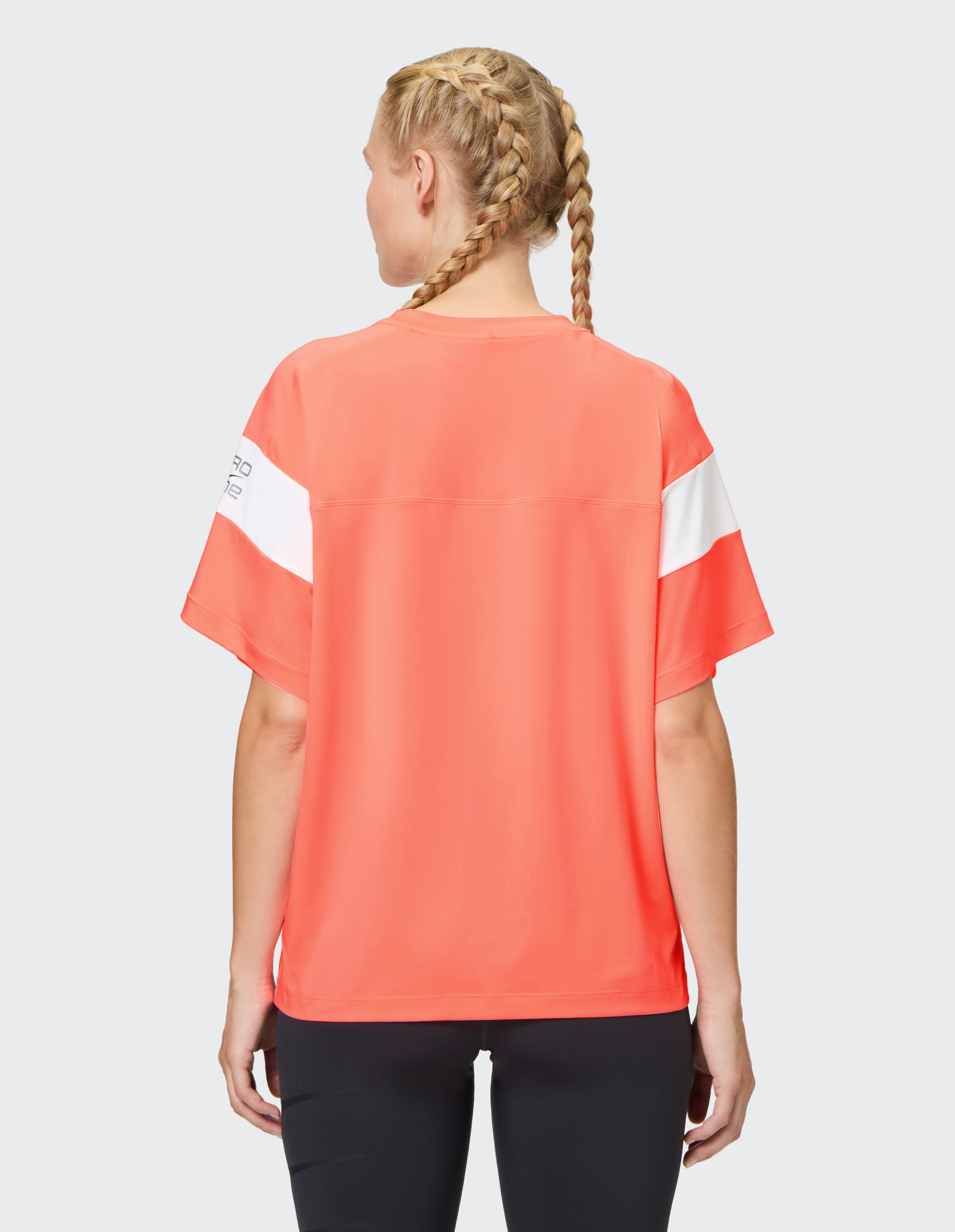 Rückansicht einer Frau, die ein korallfarbenes Freizeit-T-Shirt mit weißen Ärmelstreifen trägt.