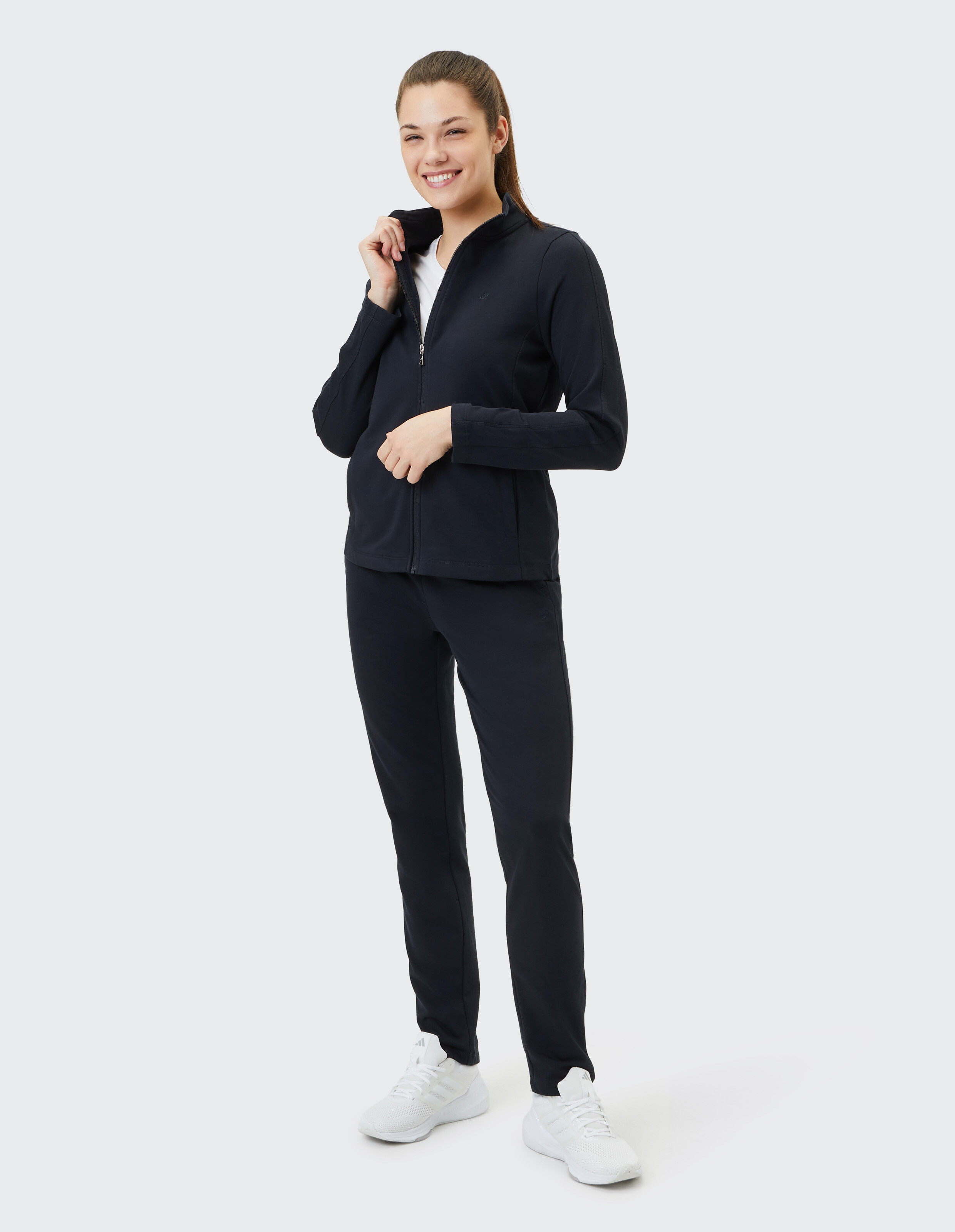 Frau in dunkelblauer, lässiger Jacke mit Reißverschluss und passender Hose, lächelnd, stilvoll und bequem.