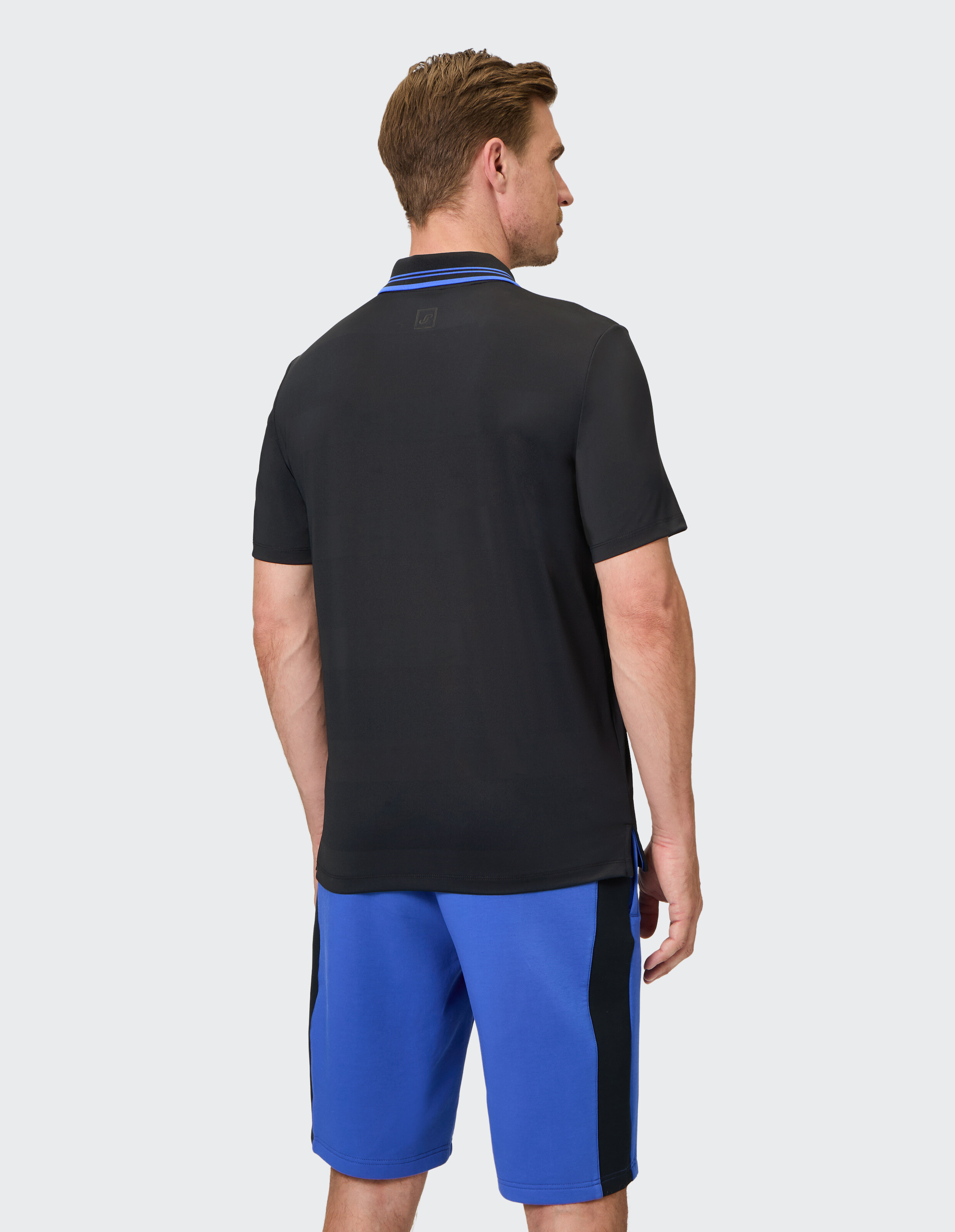 Mann trägt ein schwarzes Poloshirt mit blauen Akzenten und blauen Shorts im lässigen Stil.