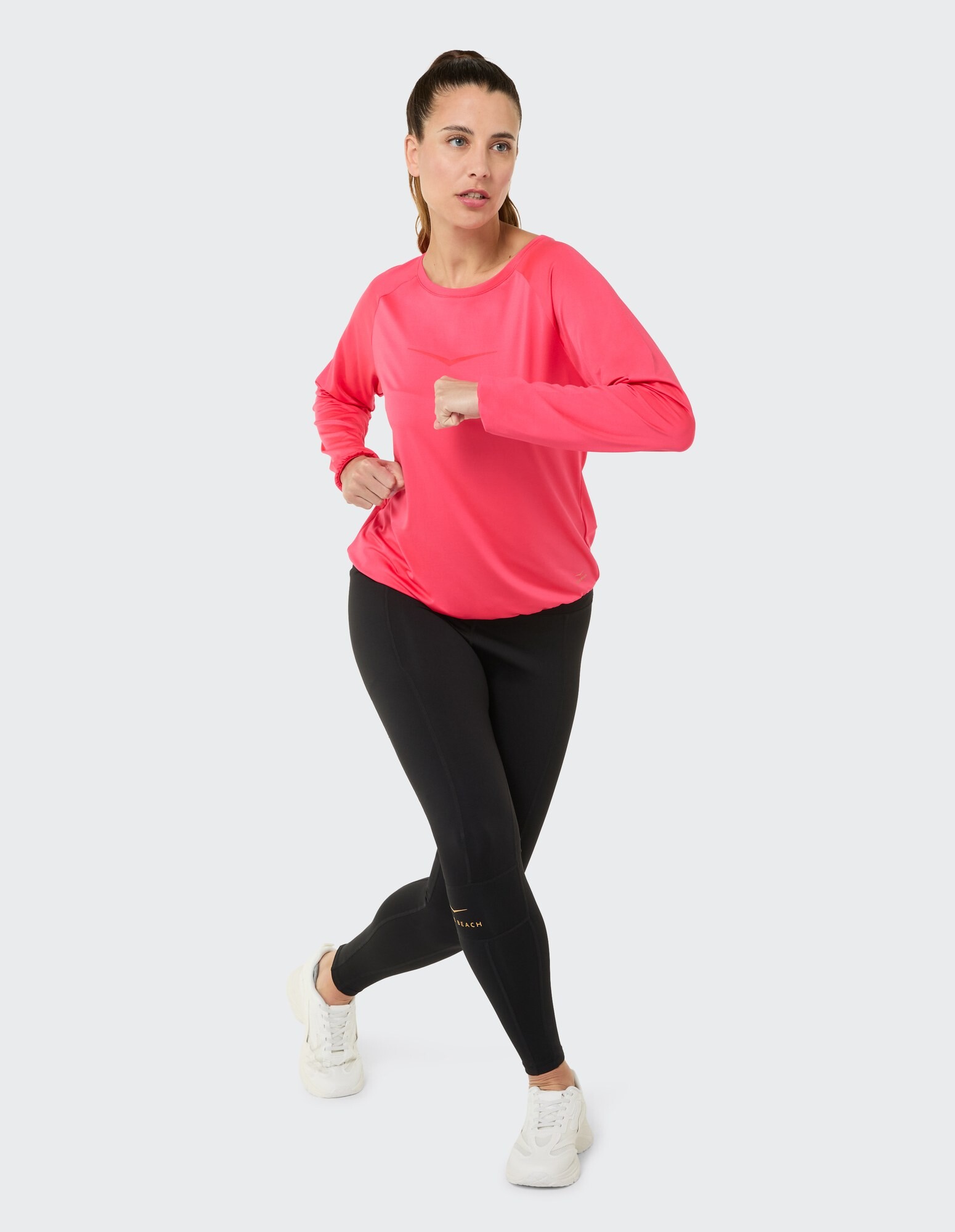 Frau in einem leuchtend rosa Langarmshirt und schwarzen Leggings, ideal für Freizeitkleidung.