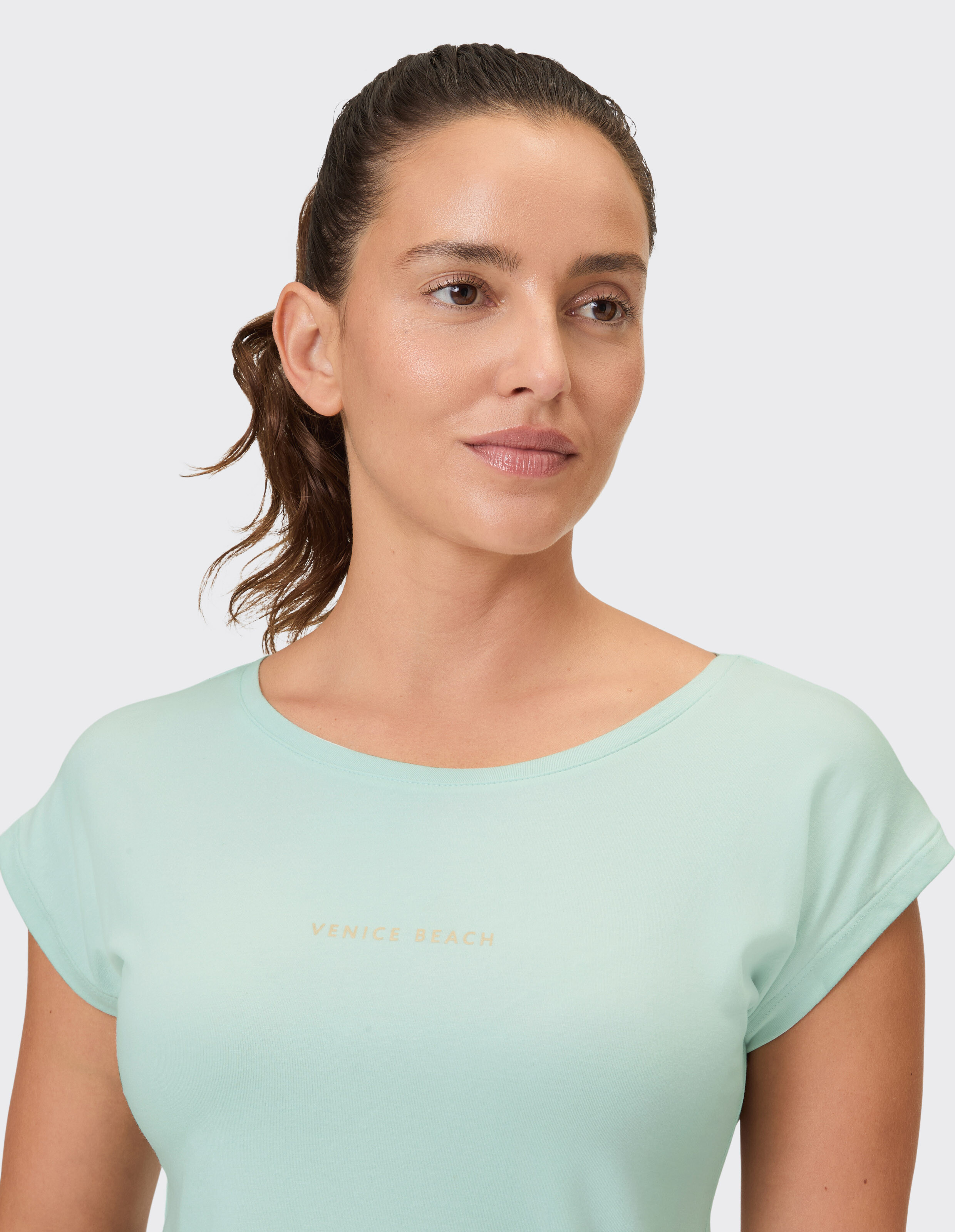 Nahaufnahme einer Frau, die ein hellmintgrünes T-Shirt mit „Venice Beach“-Aufdruck trägt.