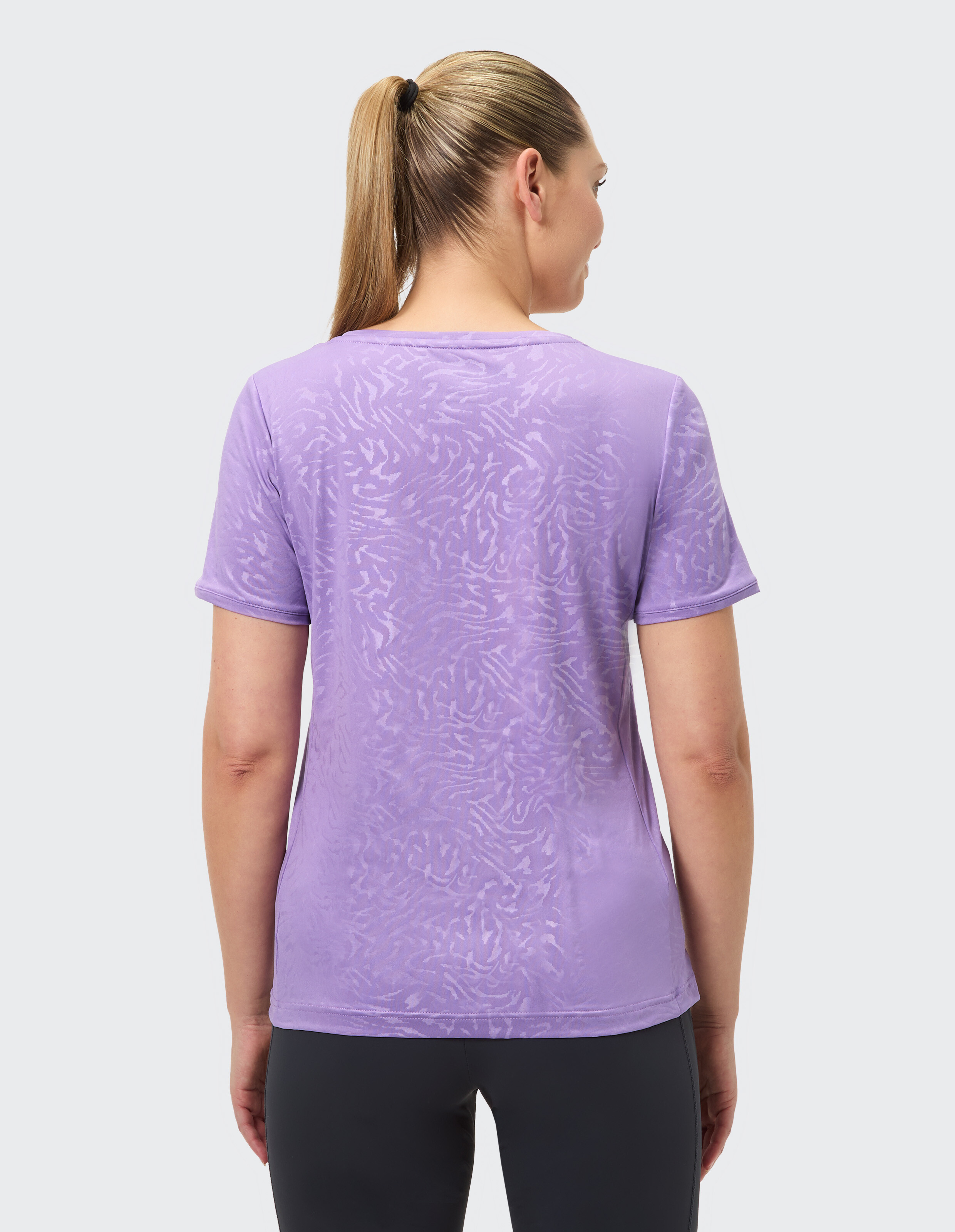 Rückansicht einer Frau in einem hellvioletten Freizeit-T-Shirt mit dezentem Muster.