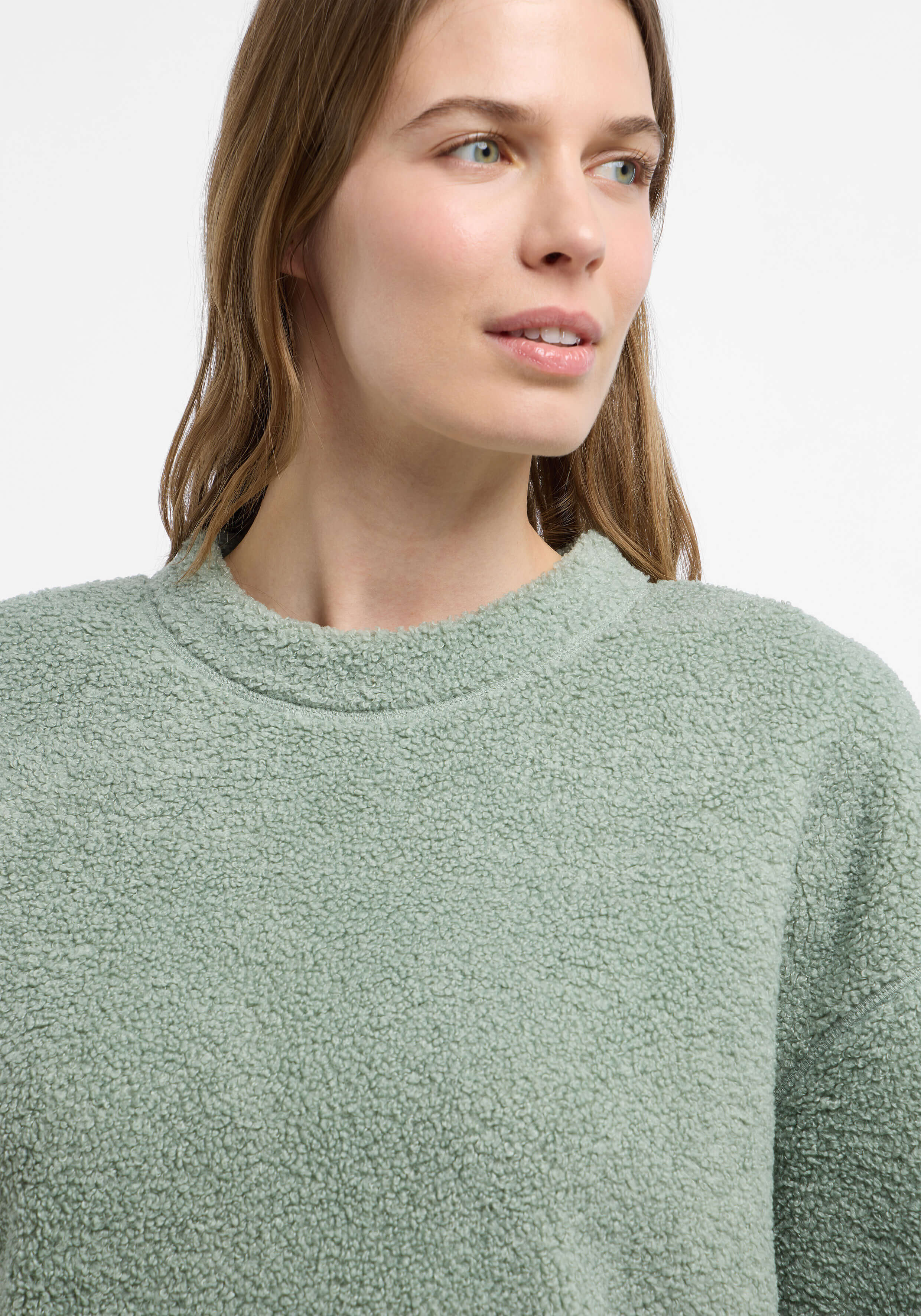 Frau trägt einen kuscheligen salbeigrünen Teddyfleece-Pullover zum entspannten Faulenzen.