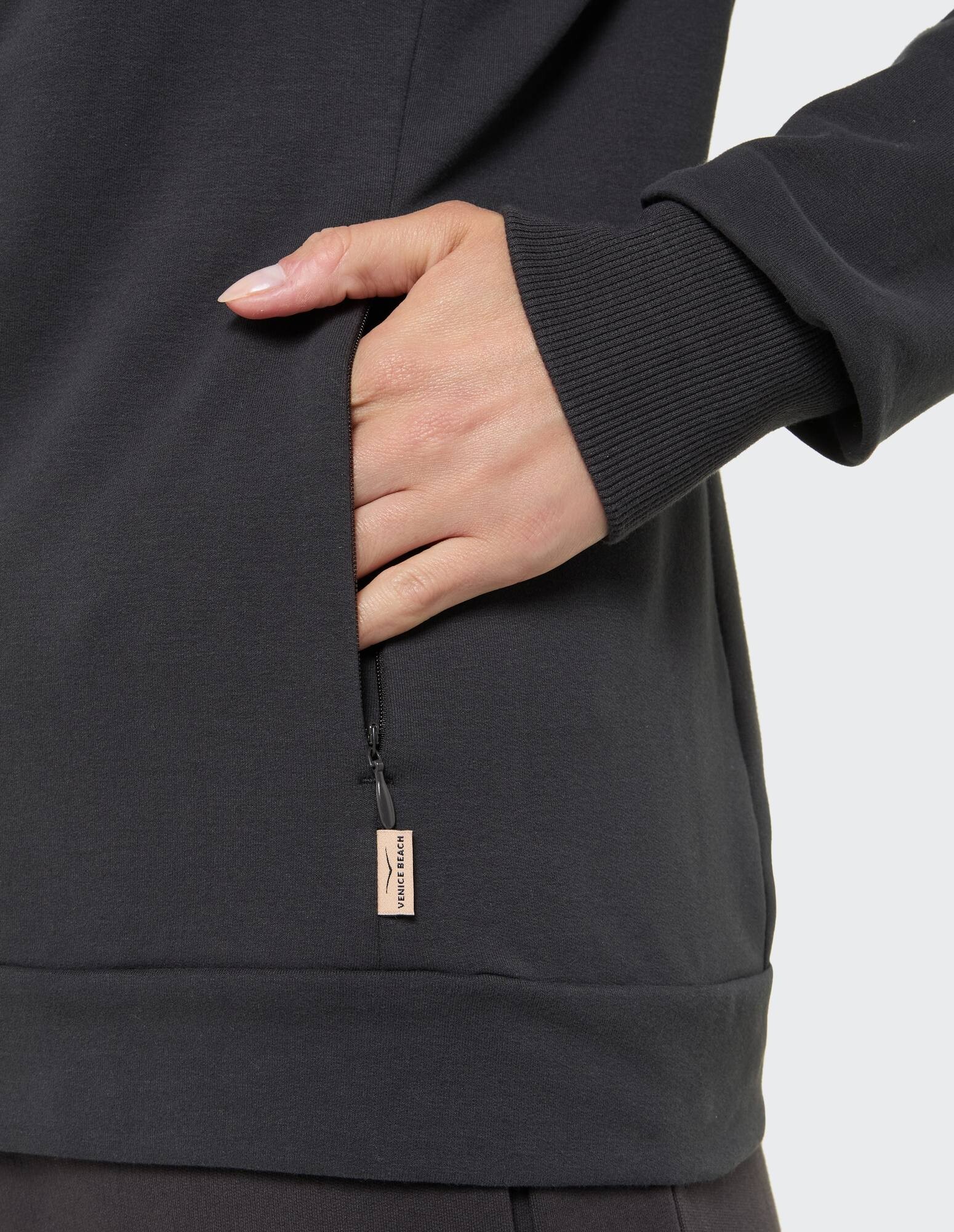 Nahaufnahme eines dunkelgrauen Sweatshirts mit Reißverschlusstasche und gerippten Bündchen.