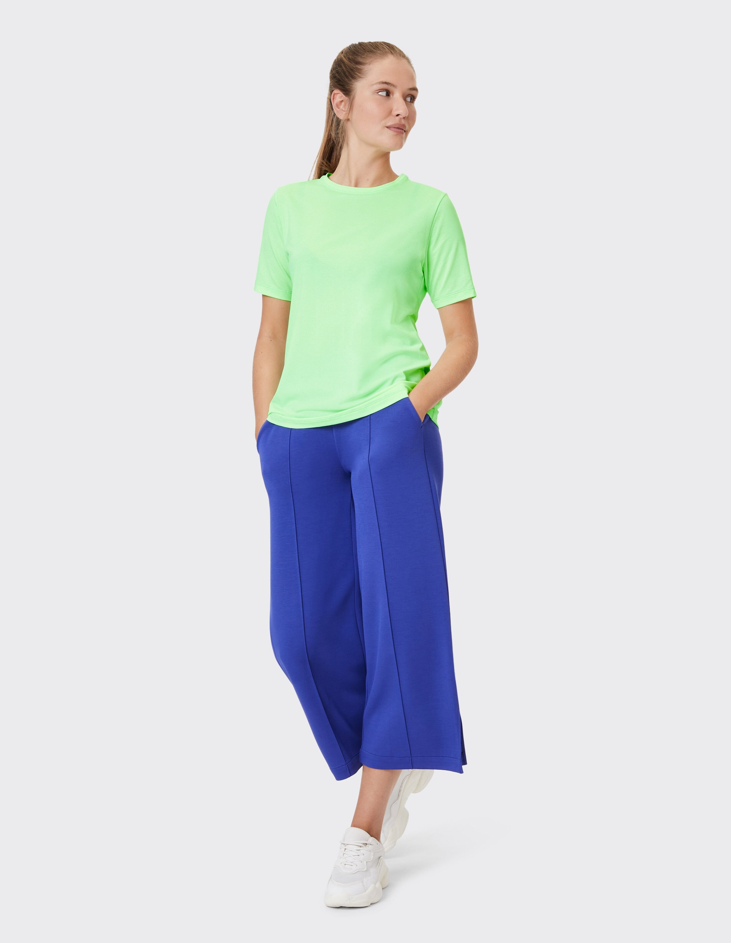 Frau in einem neongrünen T-Shirt und einer blauen Hose mit weitem Bein, lässig gestylt.