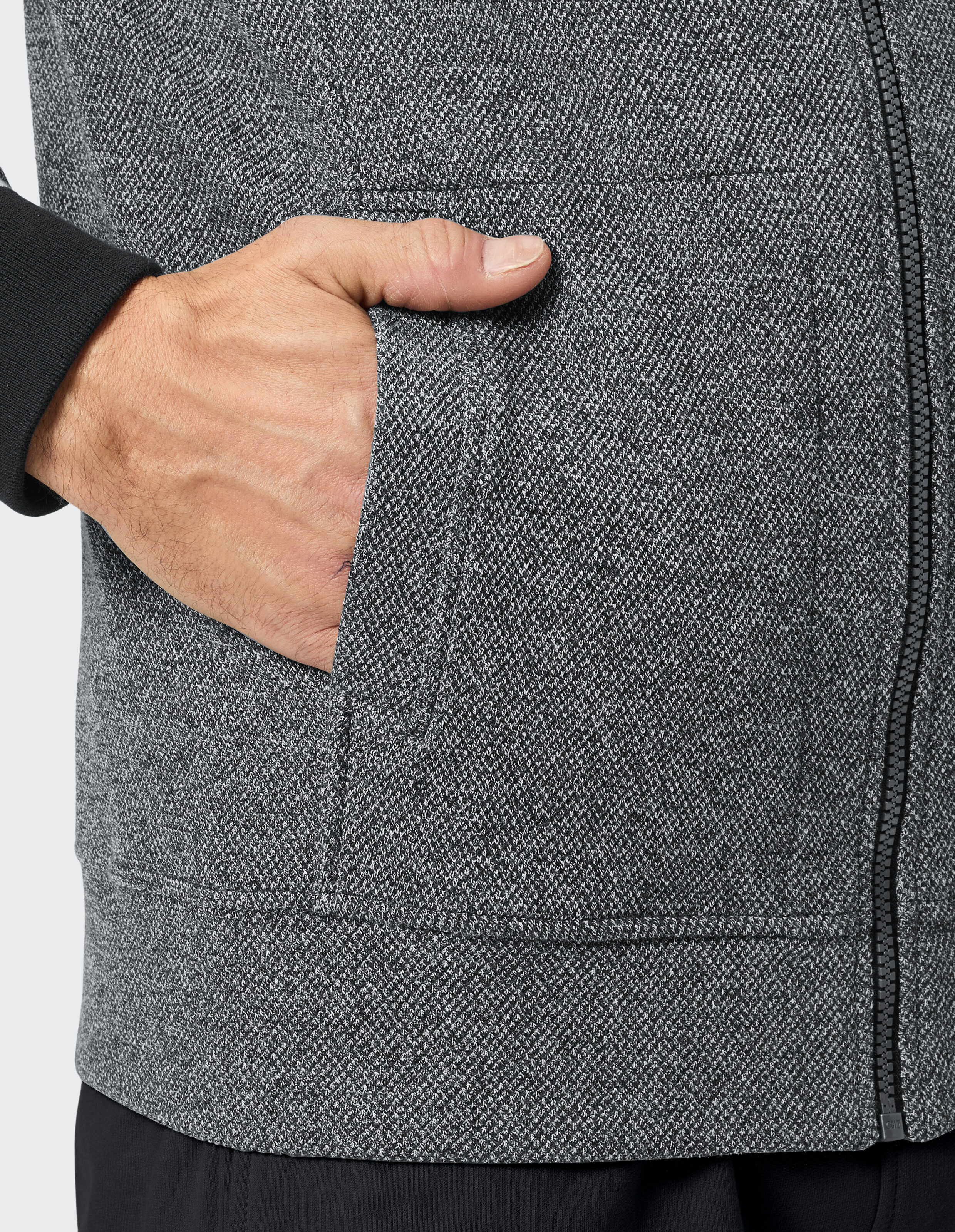 Eine Person mit einer dunklen Strickjacke mit Reißverschluss und einer Tasche.