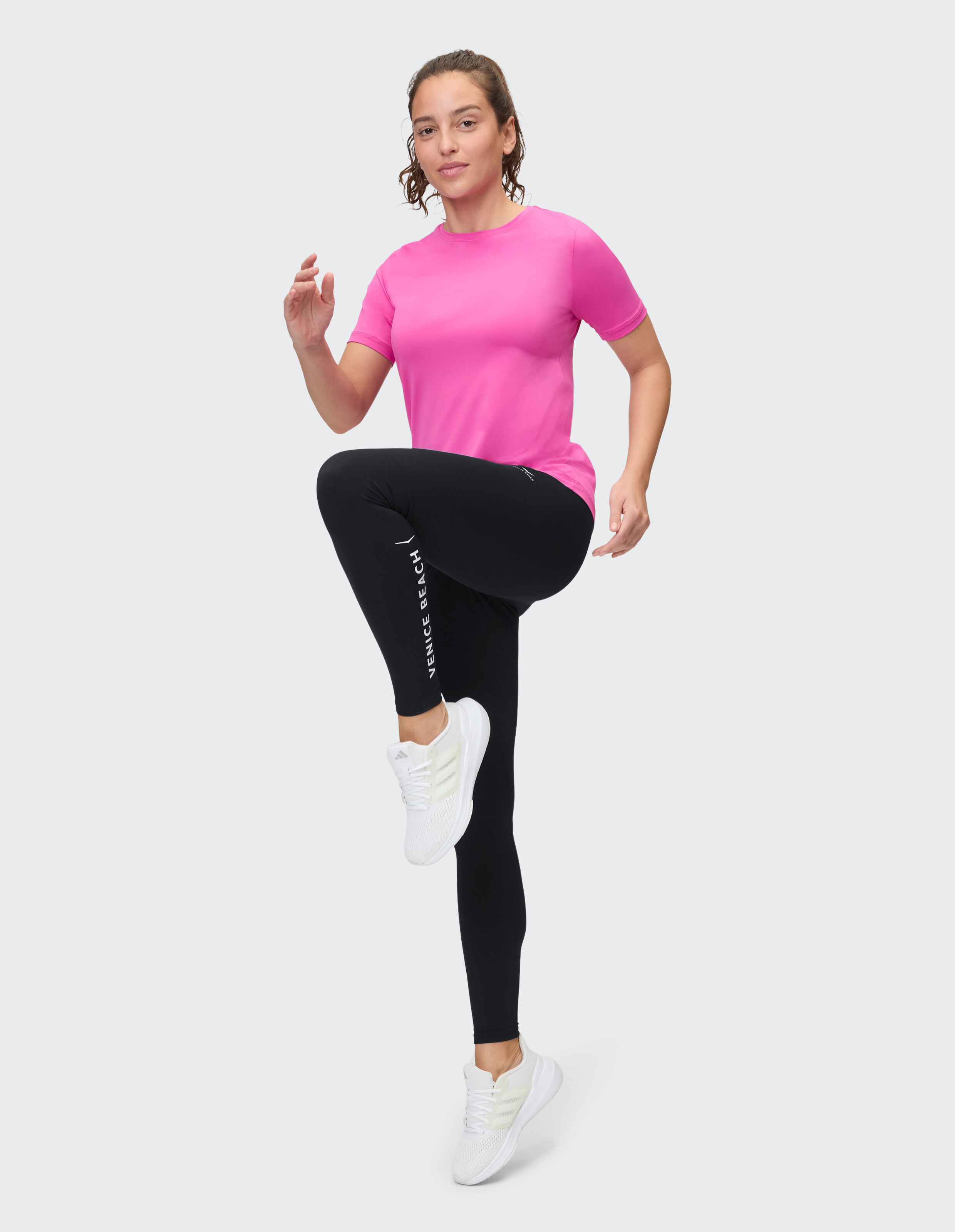 Frau in rosa T-Shirt und schwarzen Leggings im Activewear-Stil.